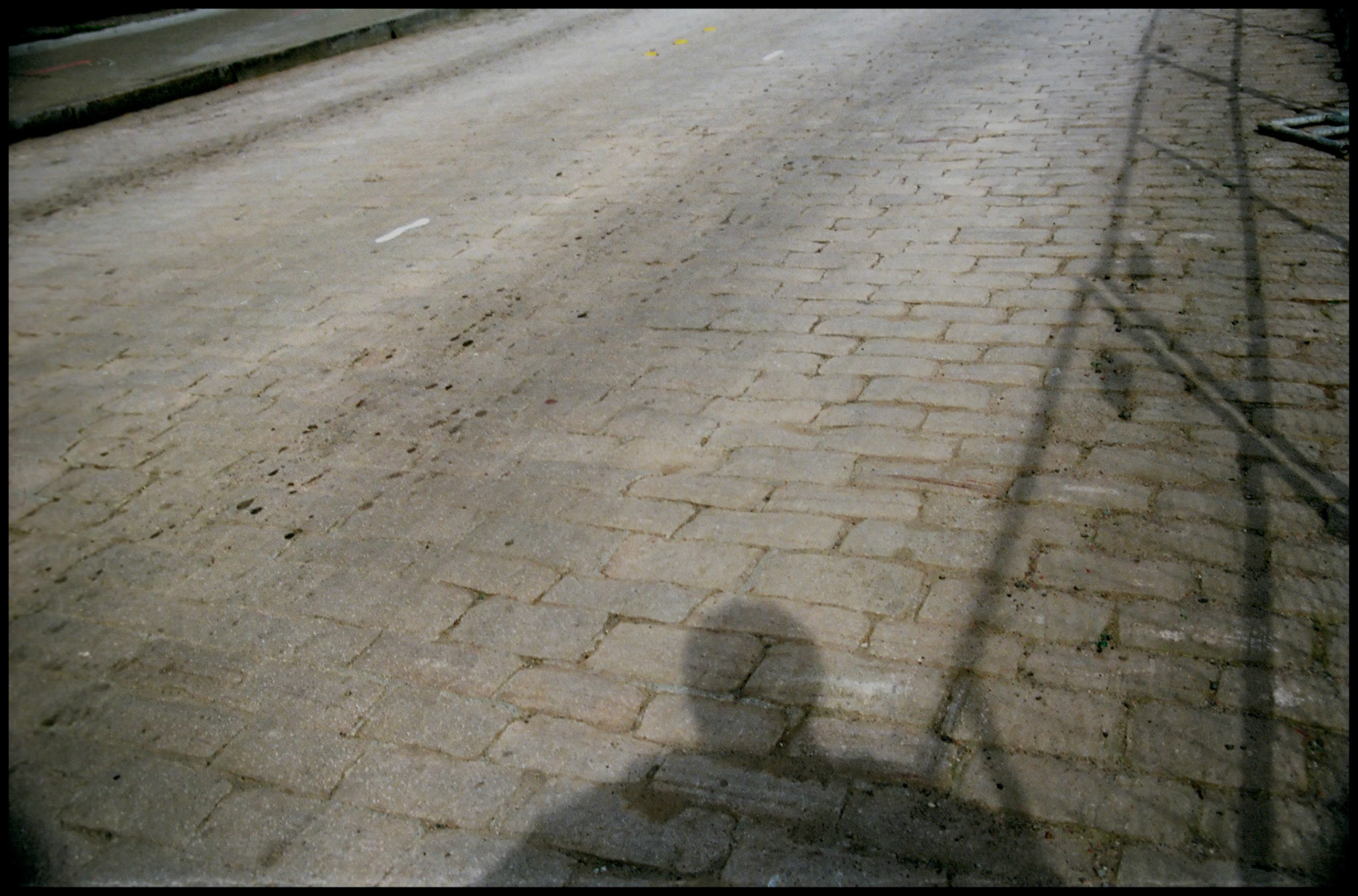A minimal conceptual abstract of a colorless brick road with the shadow of the photographer and a chain link fence. Seattle Washington, 1987
