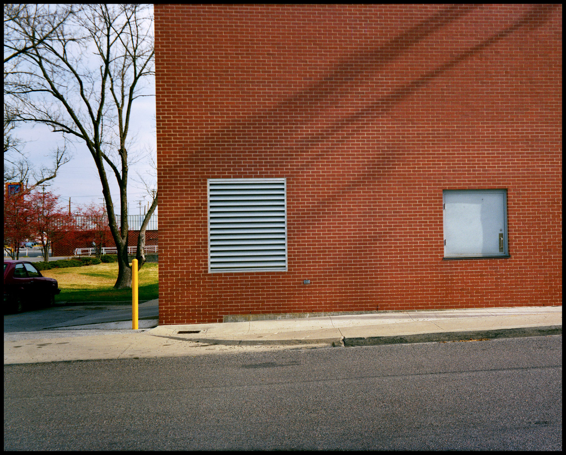 A minimal abstract detail of vent, door and safety bollard on the red brick wall of the Pepsi building in Columbia, Missouri 1989