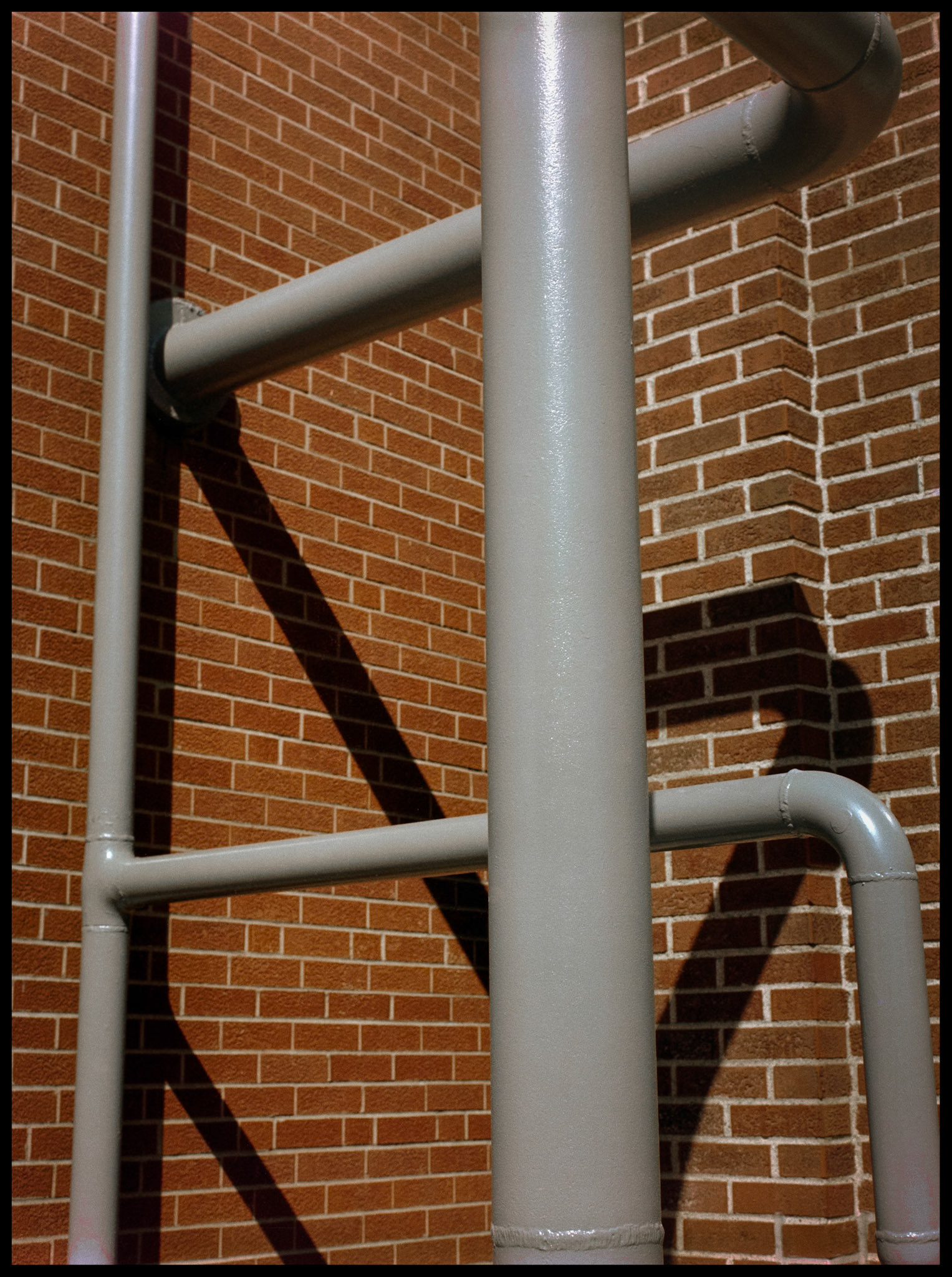 A minimal abstract detail of pipes and their shadow against a brick wall on Northeast Missouri State University (Since renamed Truman State University) campus. Kirksville, Missouri 1981