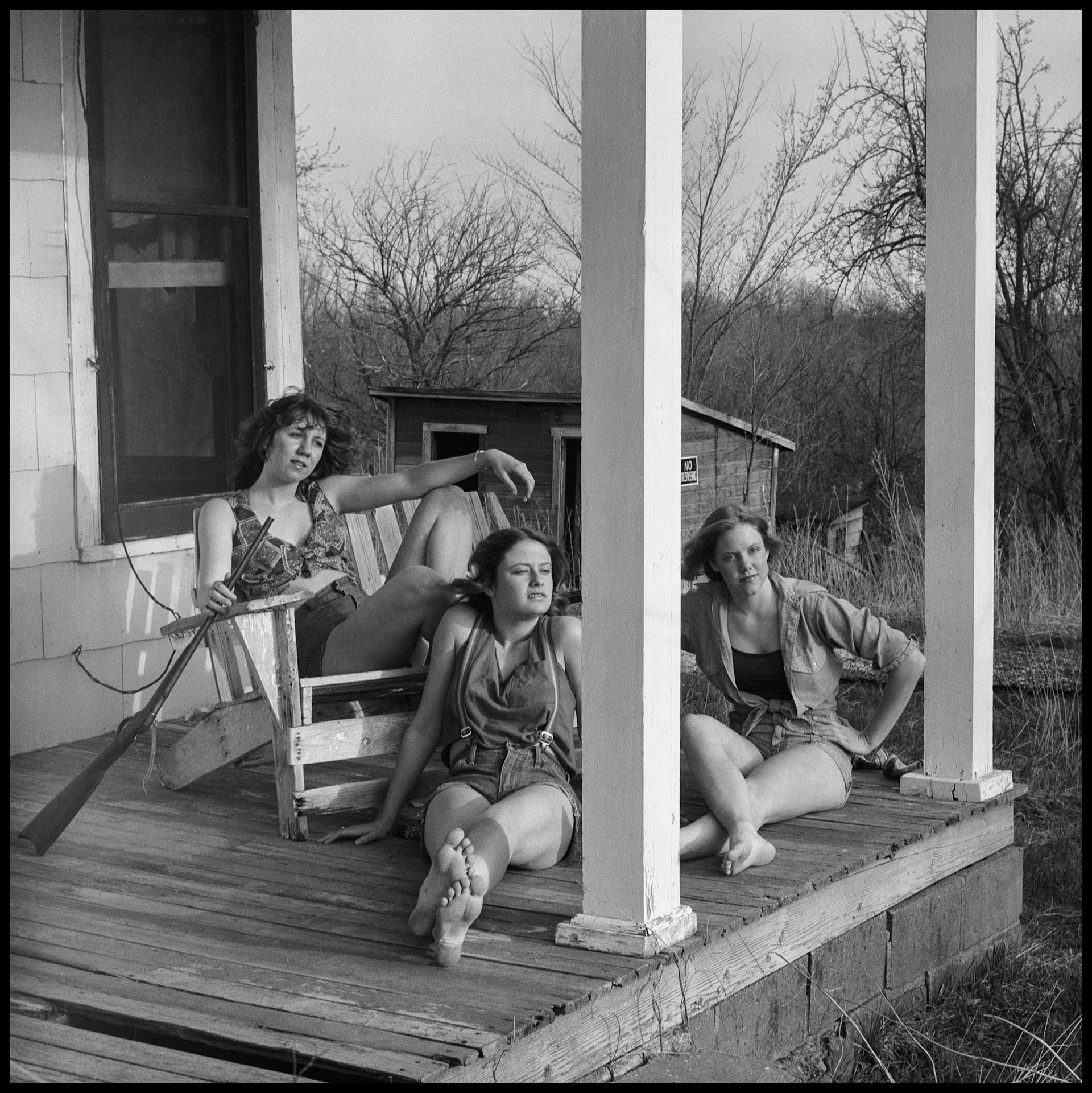 A vintage image of three teenage girls posing as hillbilly girls with props in front of an abandoned house. Kirksville Missouri 1978
