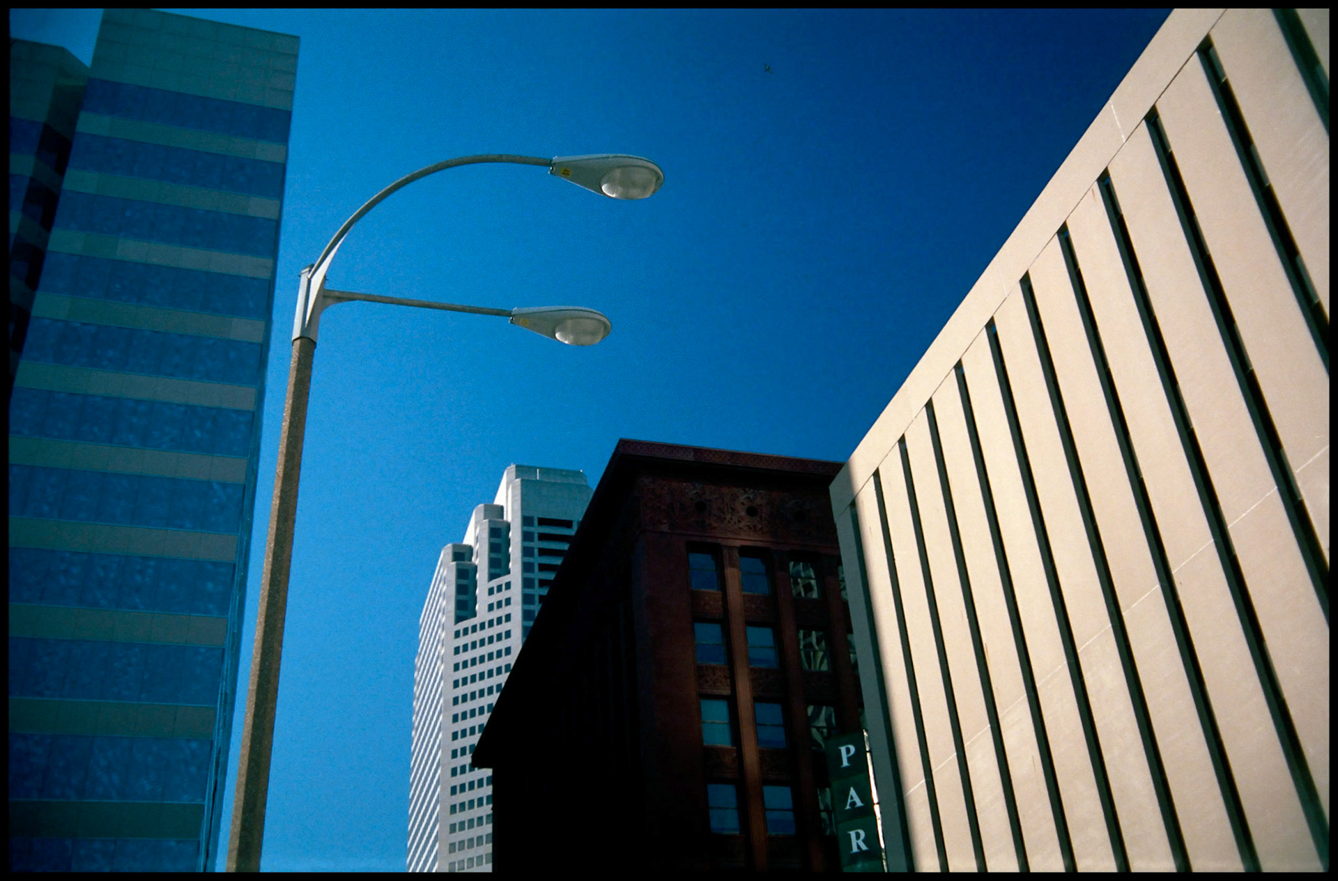A streetlight seemingly looming over adjacent buildings. Part of a series shot one warm afternoon in November, 1988 called An Afternoon in St. Louis (a subset of my Industrial Geometry series).