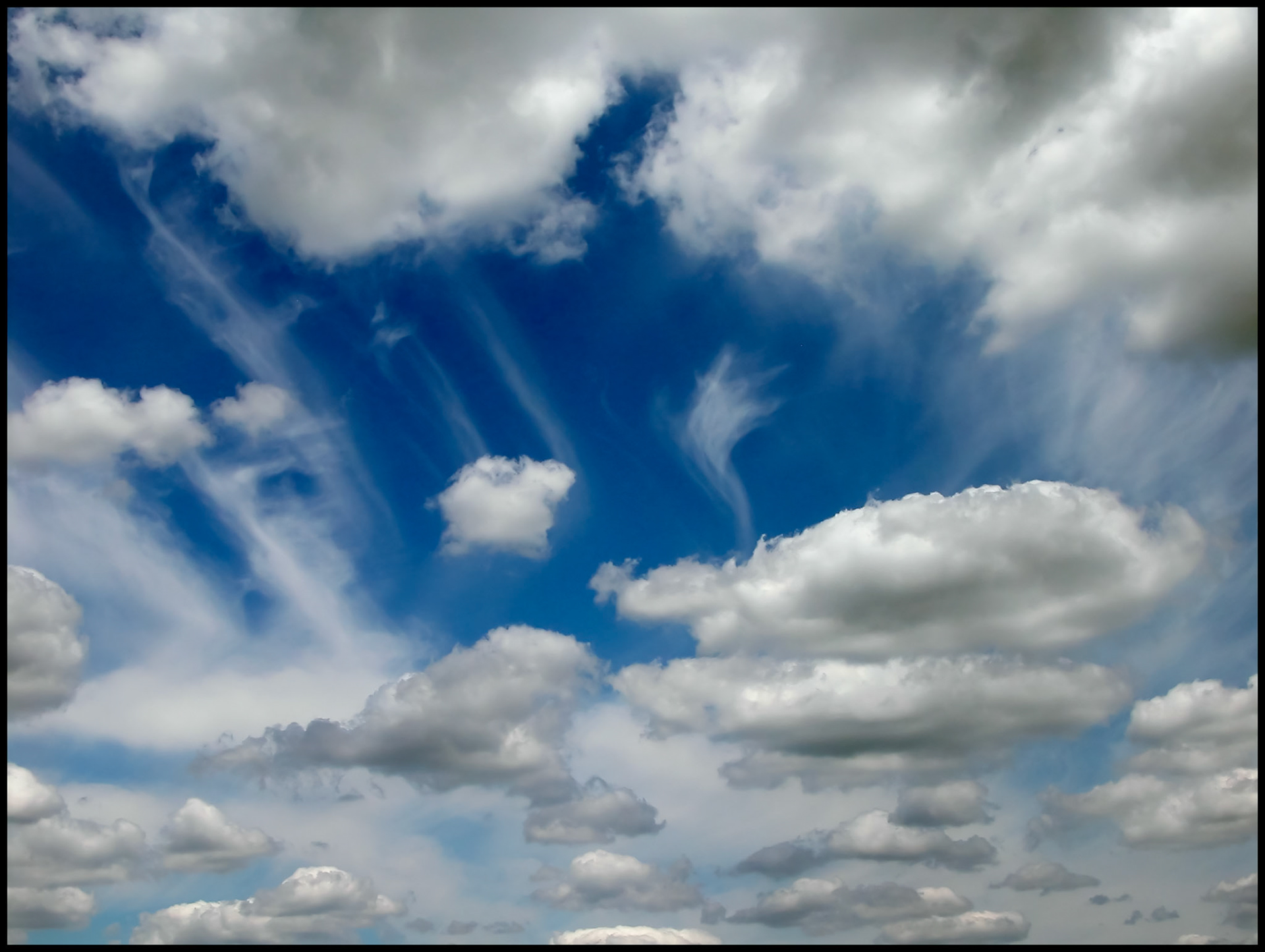 Wispy cirrus clouds shooting out diagonally behind stratus clouds contrasted by a dark blue sky in Centralia Missouri. 2003