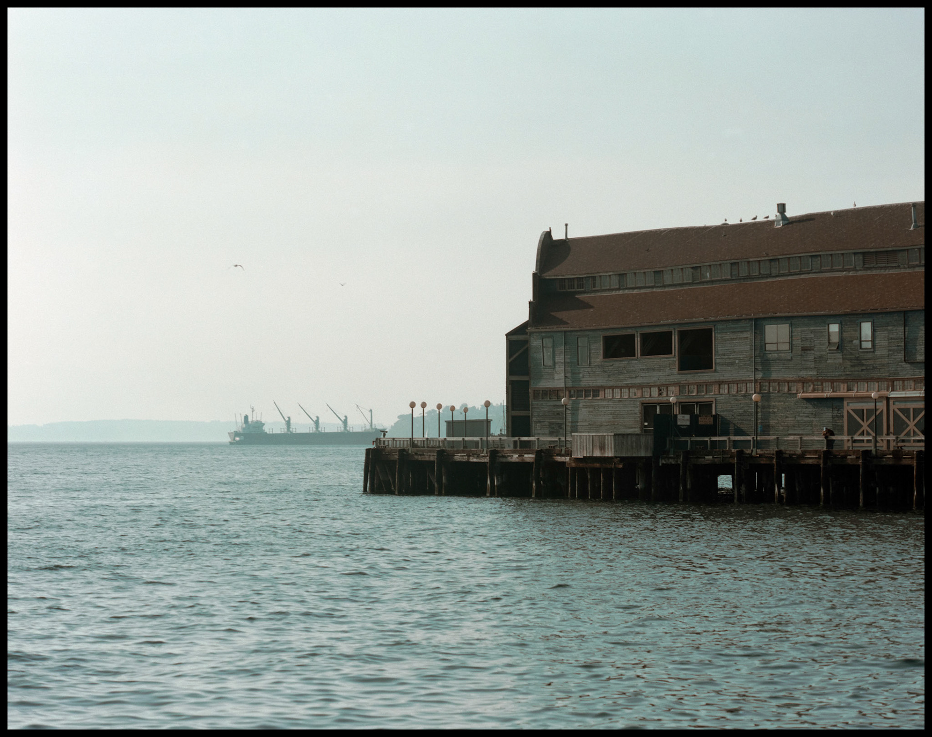 A vintage waterside view of the South side of the building that is now the Seattle Aquarium from an adjacent pier with a ship in the background. Seattle Washington USA 1987