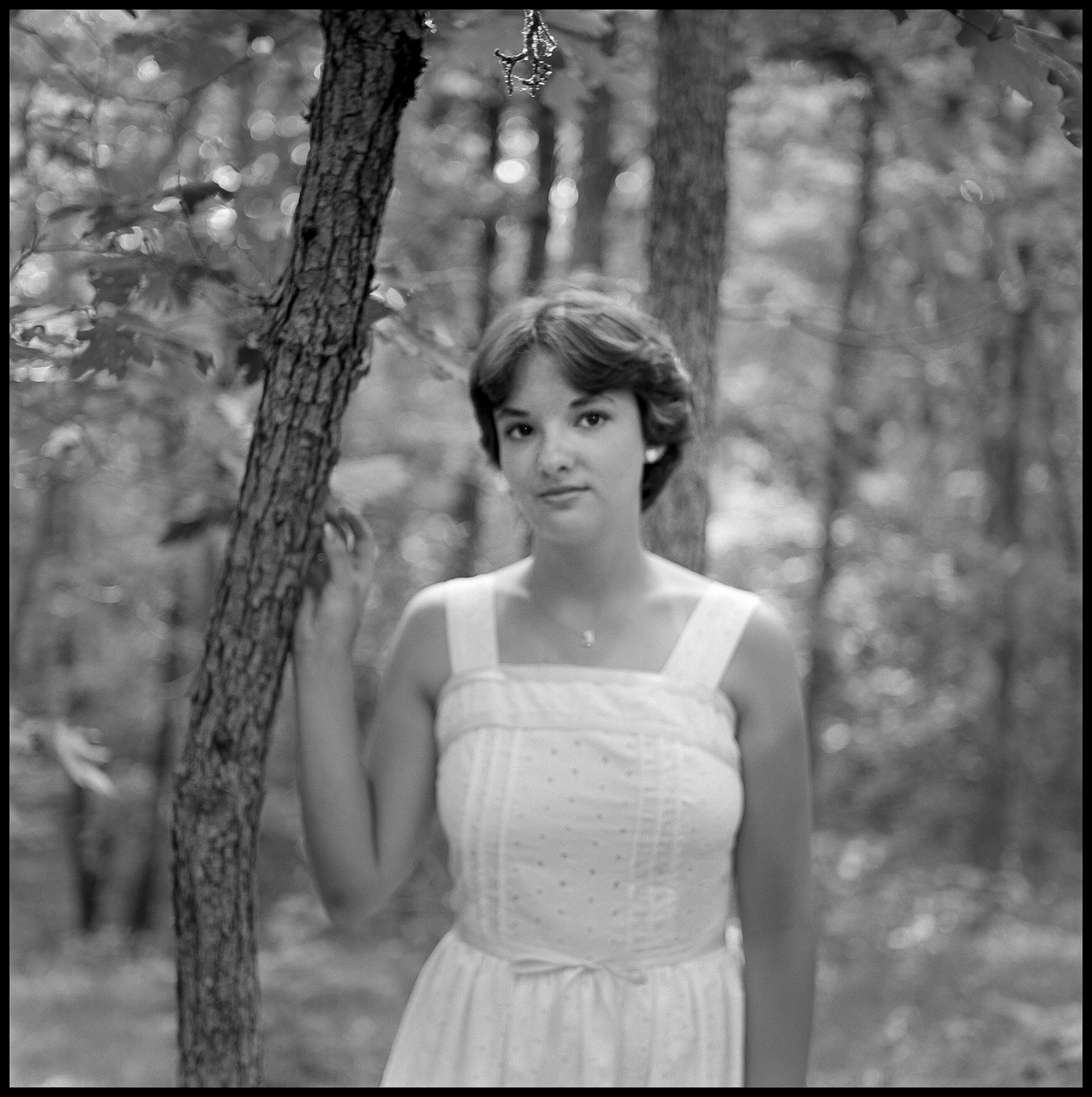 A 1970's vintage soft focus image of a young woman leaing on a tree in a forest with a thoughtful expression. Kirksville, Missouri 1978