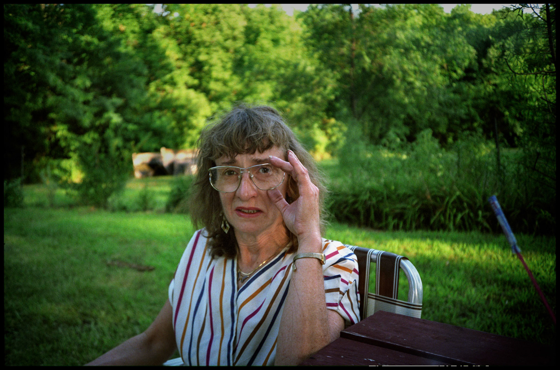 A middle aged woman grips her glasses as she stares intently at the camera and grimaces during a July 4th picnic. Near Kansas City, Missouri 1991