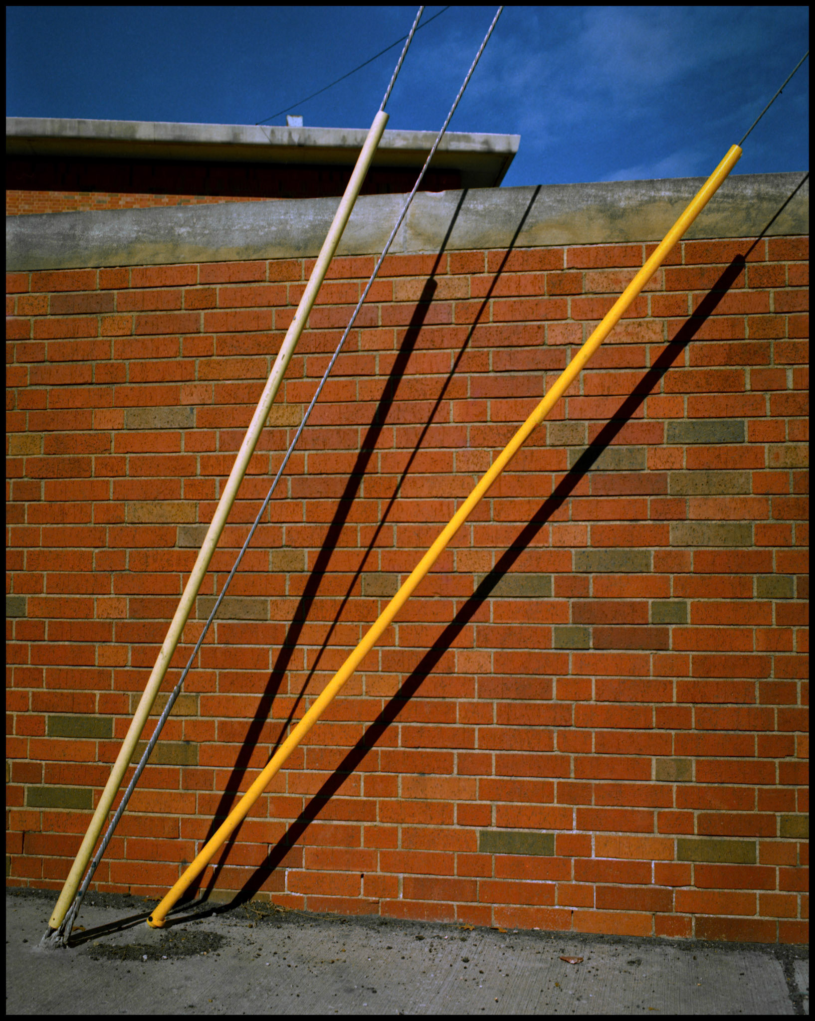 An minimal abstract detail view of guy wires from a utility pole next to a red brick wall with interesting shadows. Columbia Missouri 1990