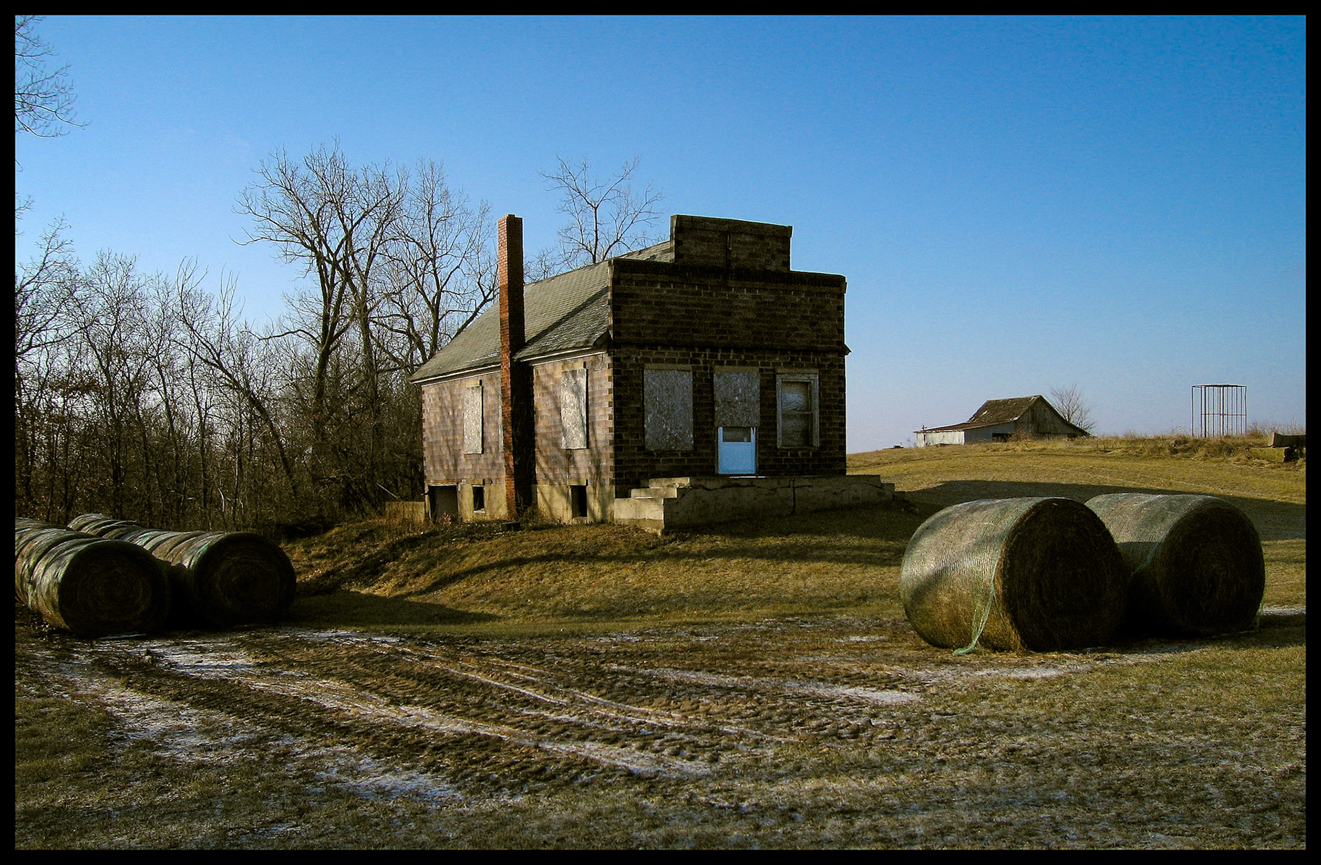 A boarded up country store building in Pure Air, Missouri surrounded by hay bales with a barn in the background. 2007