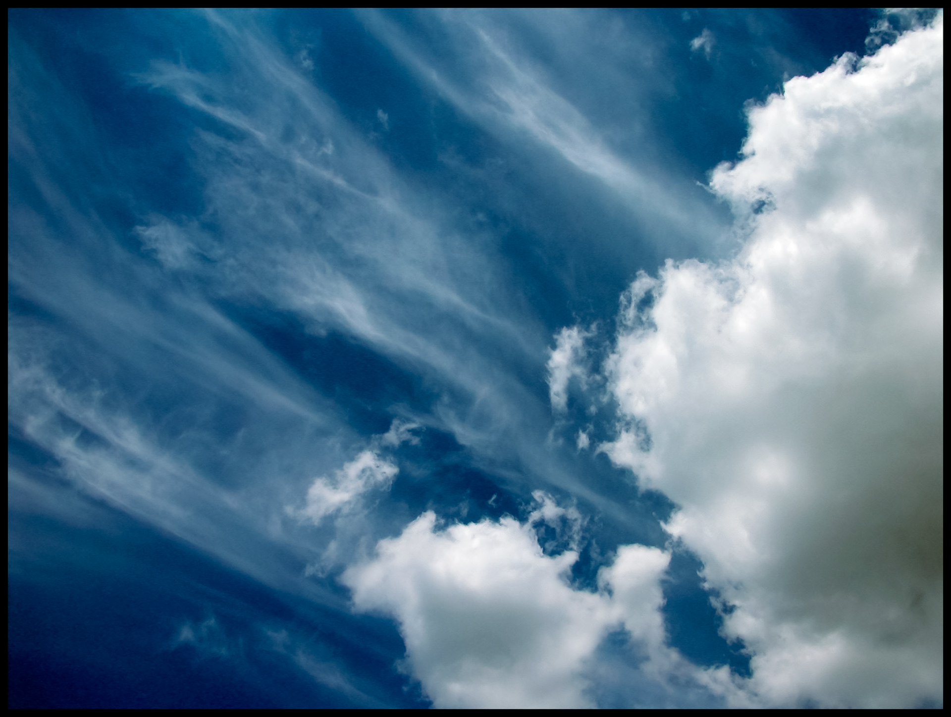 Whispy cirrus clouds shooting out diagonally behind stratus clouds contrasted by a dark blue sky in Centralia Missouri