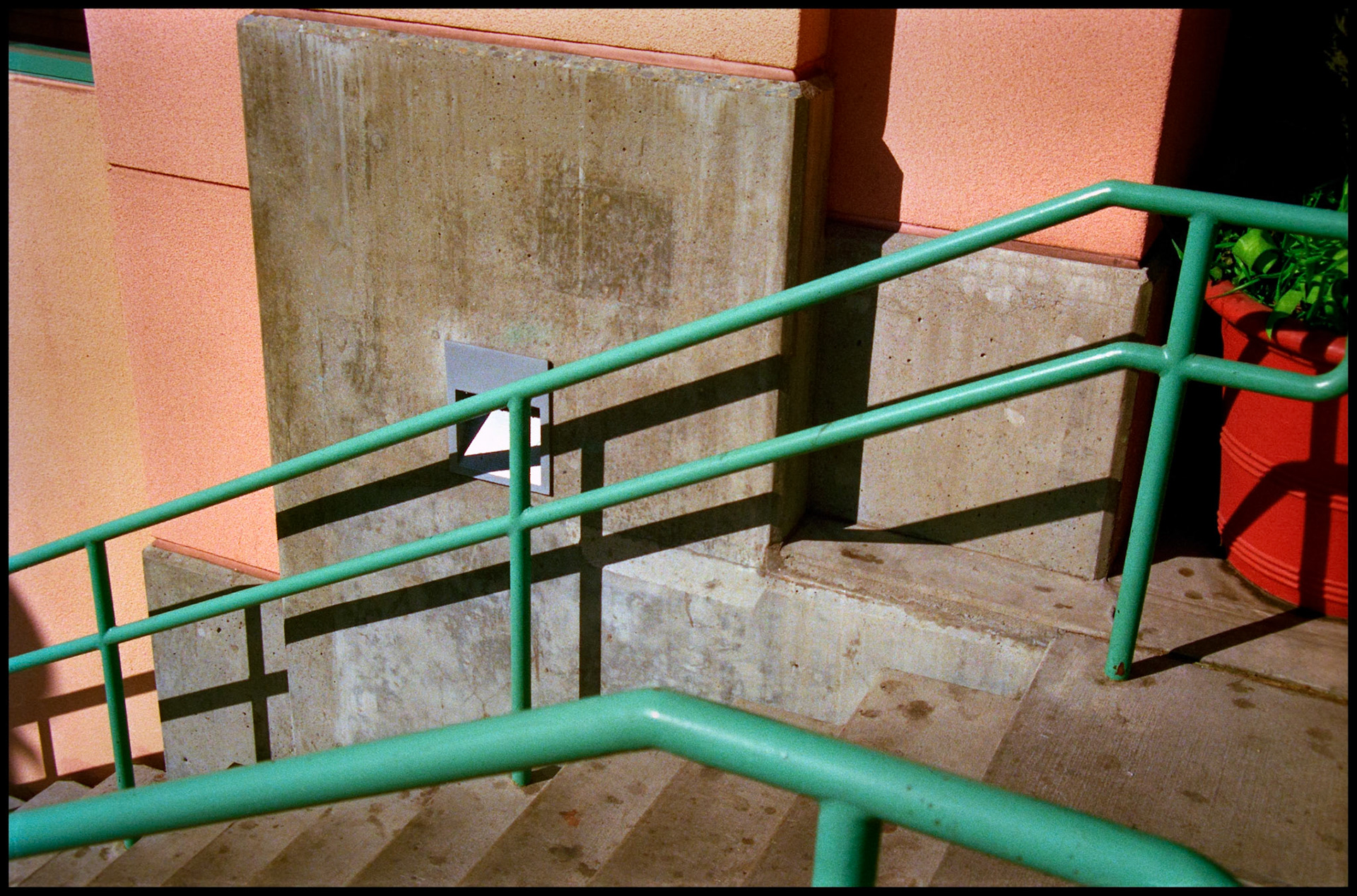 A minimal abstract view of a colorful handrail and concrete stairs next to a colorful wall of a building. Seattle, Washington 1987