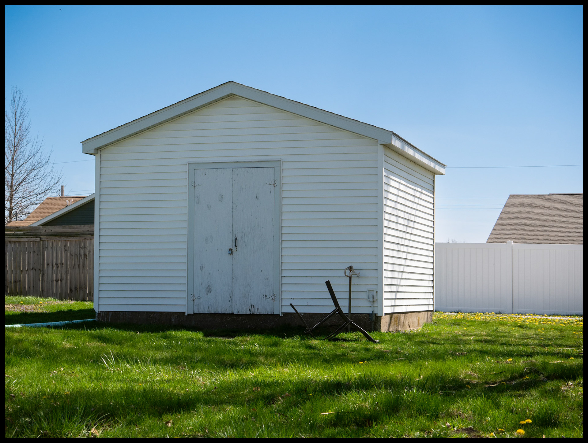 A suburban backyard shed with an overturned chair in front in springtime. Kirksville, Missouri, 2024.