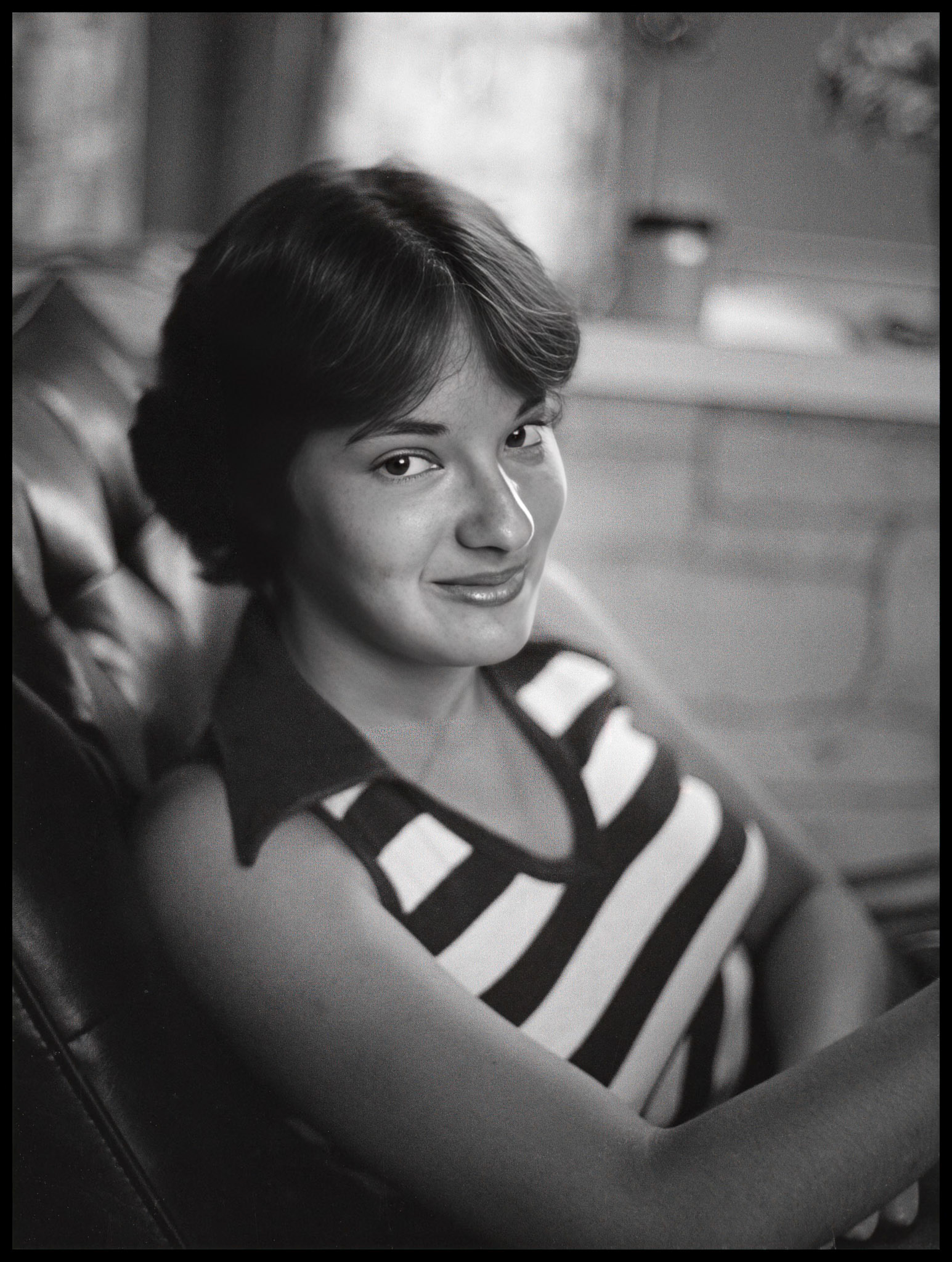 A young woman sitting in a living room chair with a mischevious smile, 1978.