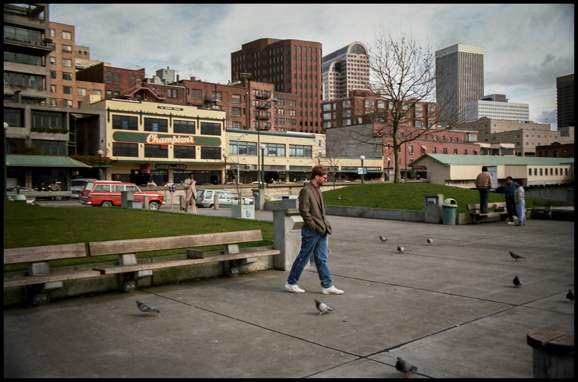 A vintage street scene of a man walking amongst pigeons on sidewalk at Pike Place Market near the waterfront in Seattle, Washington 1987