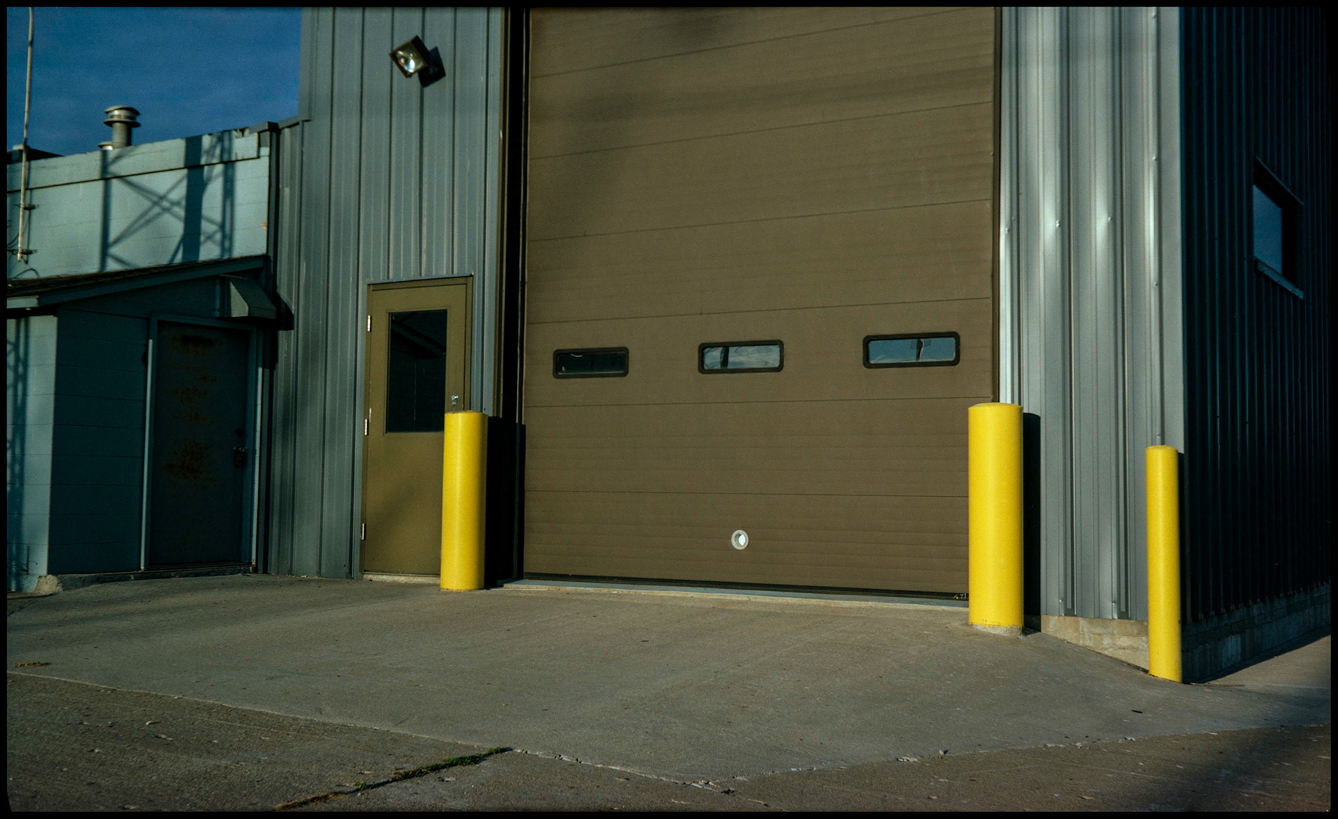 Yellow safety bollards in front of a brown door on a commercial building. Columbia, Missouri 1989