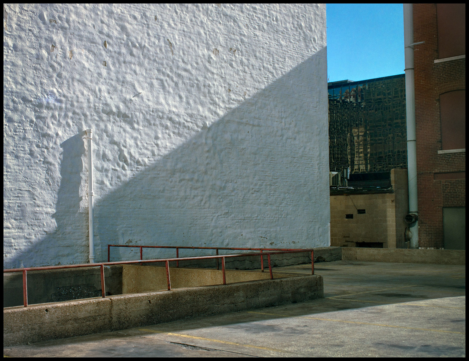 An abstract minimal detail of a triangular shadow on a white stucco wall at the edge of a parking lot in downtown St. Louis, Missouri 1988. Part of a series shot one afternoon in November, 1988 called An Afternoon in St. Louis (a subset of my Industrial Geometry series).
