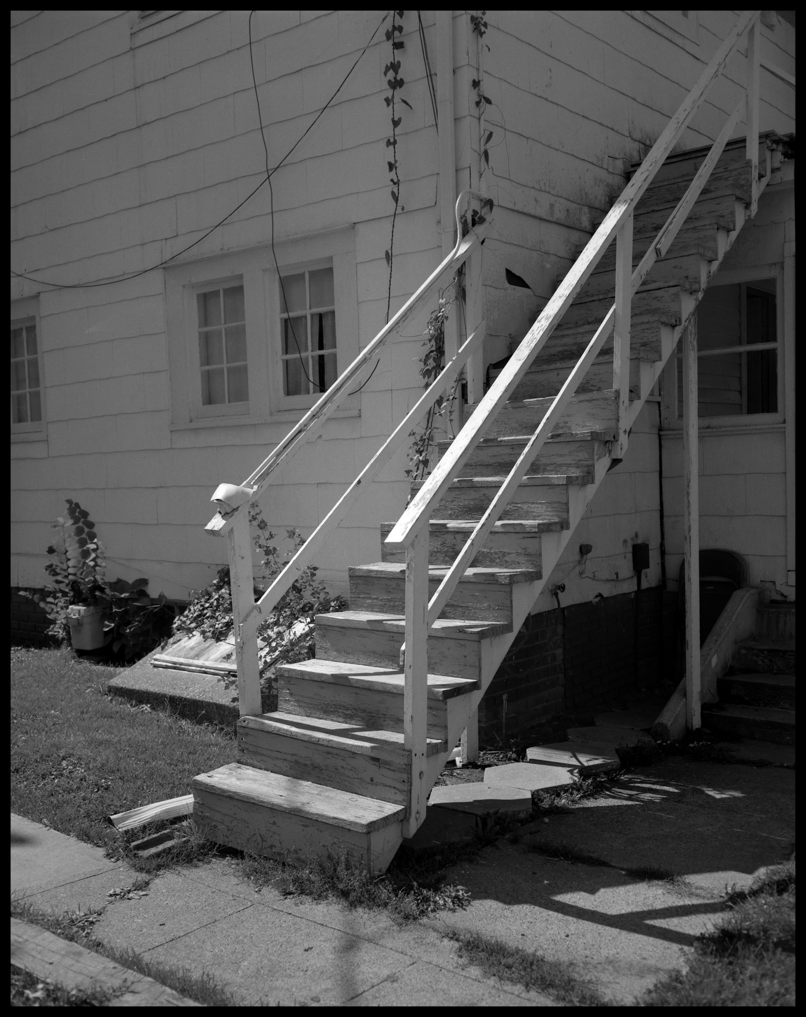 The handrails of a wooden stairway of an older house converted to apartments highlighted by the mid day summer sun. Kirksville, Missouri, 1984.