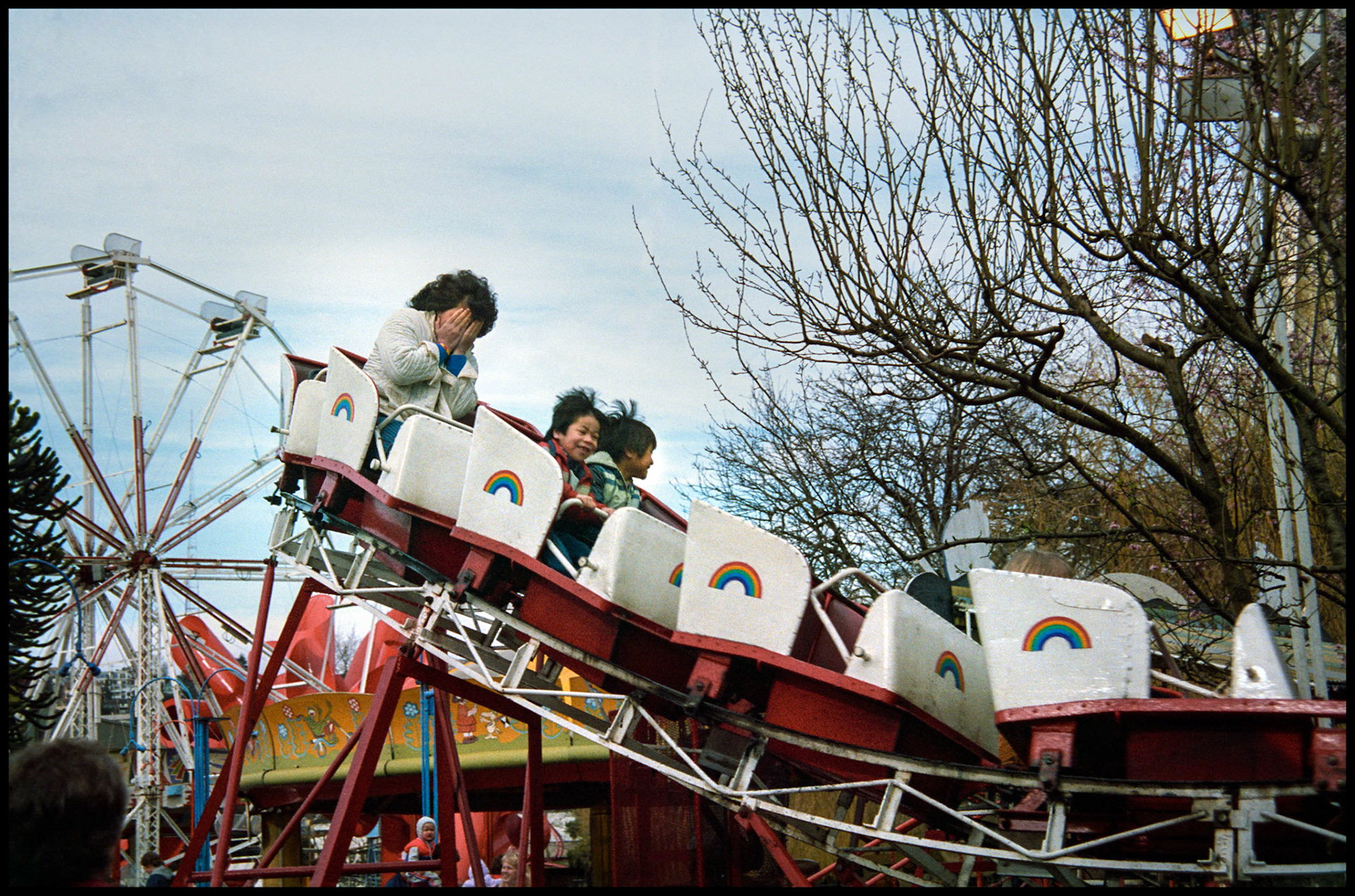 A vintage street scene of two kids and a mother on a kiddy size roller coaster where the kids are having fun and the mother is terrified. Street carnival near the Space Needle in Seattle Washington USA 1987