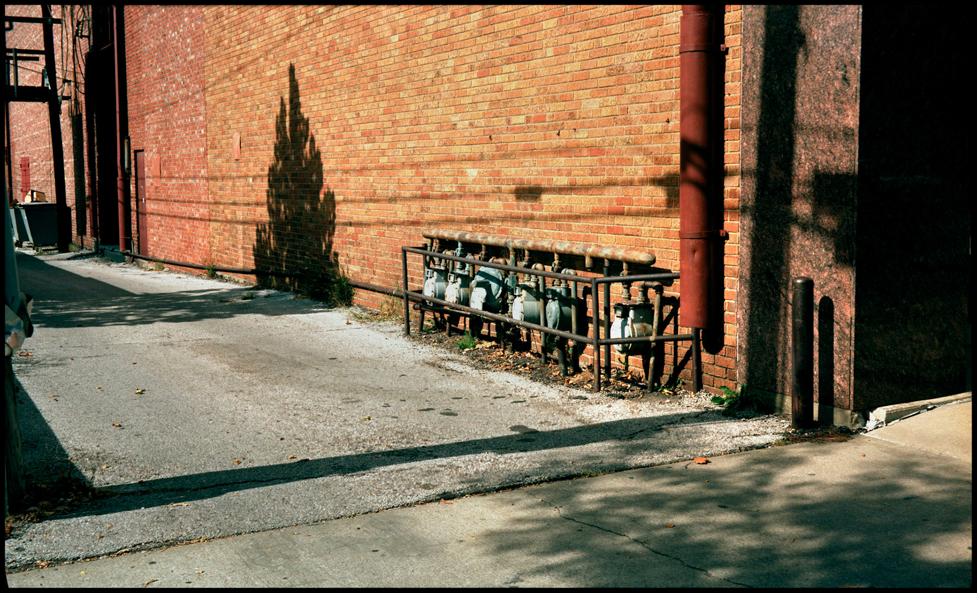 An urban alley with an interesting  shadow of a tree on the red brick wall next to a row of gas meters. Columbia, Missouri 1989