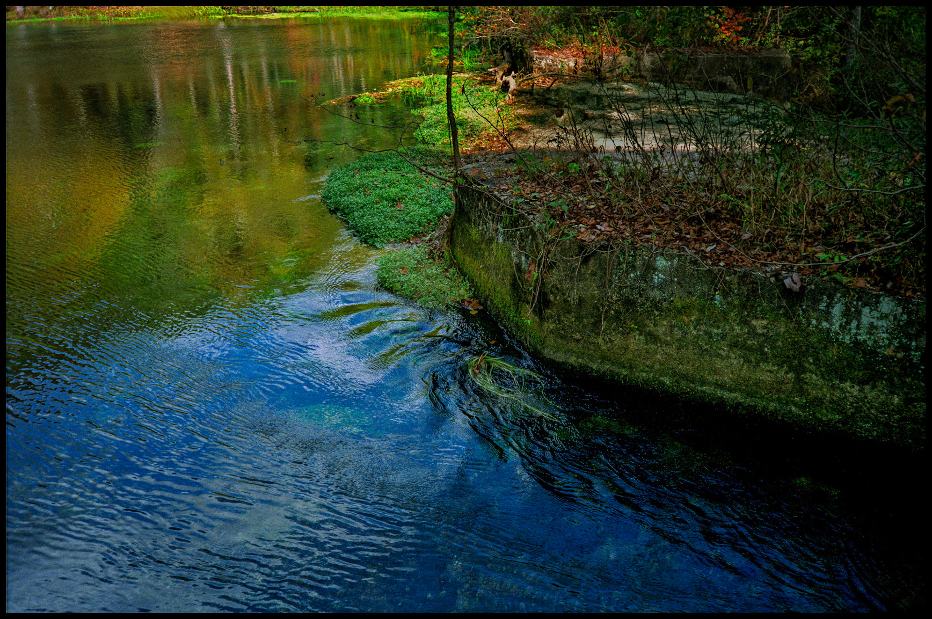A minimal abstract detail of the brilliant colored reflections on the deep blue water flowing into Alley Spring Mill from Alley Spring near Eminence, Missouri USA,1991