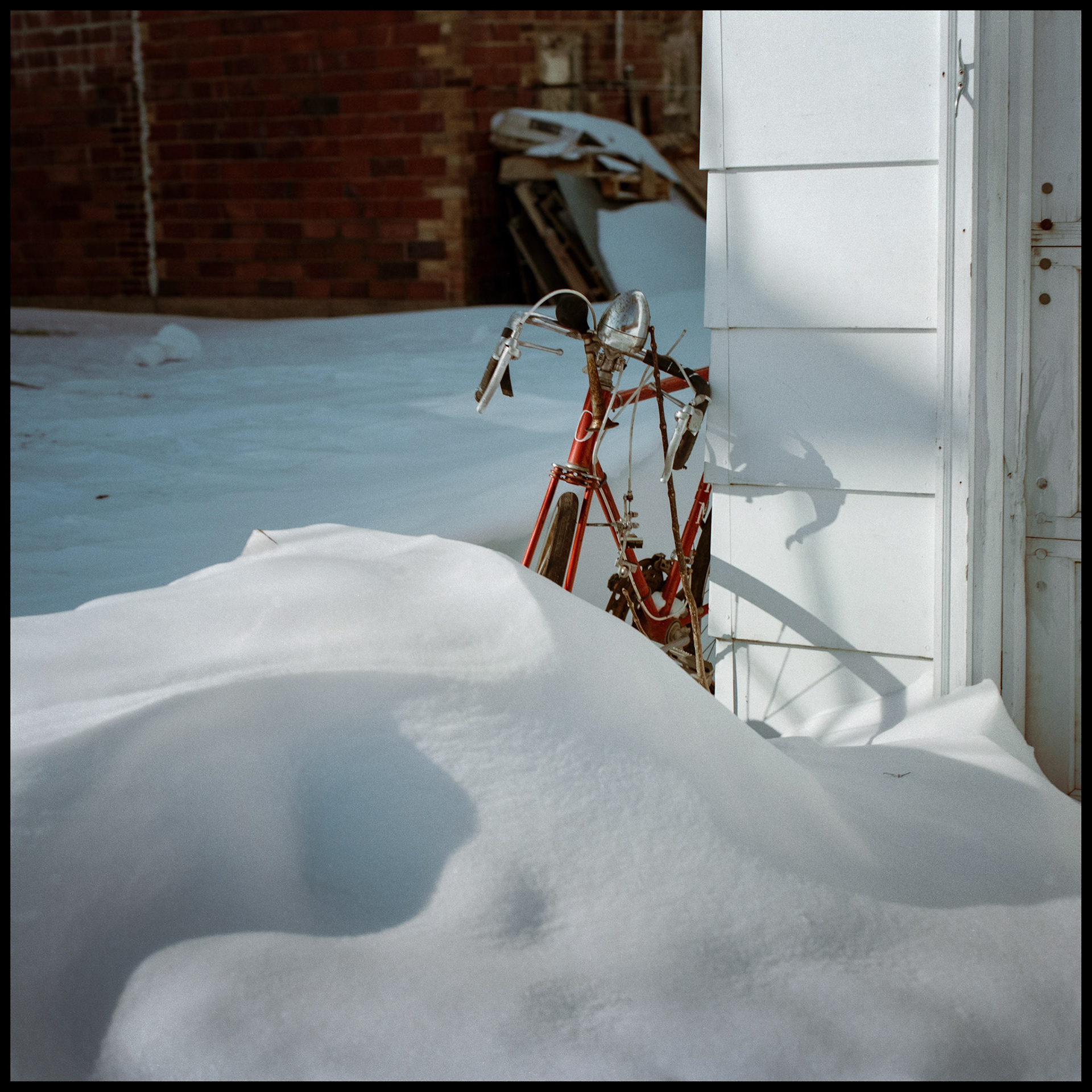A red bicycle embedded in a snow drift next to a garage. Kirksville, Missouri 1985