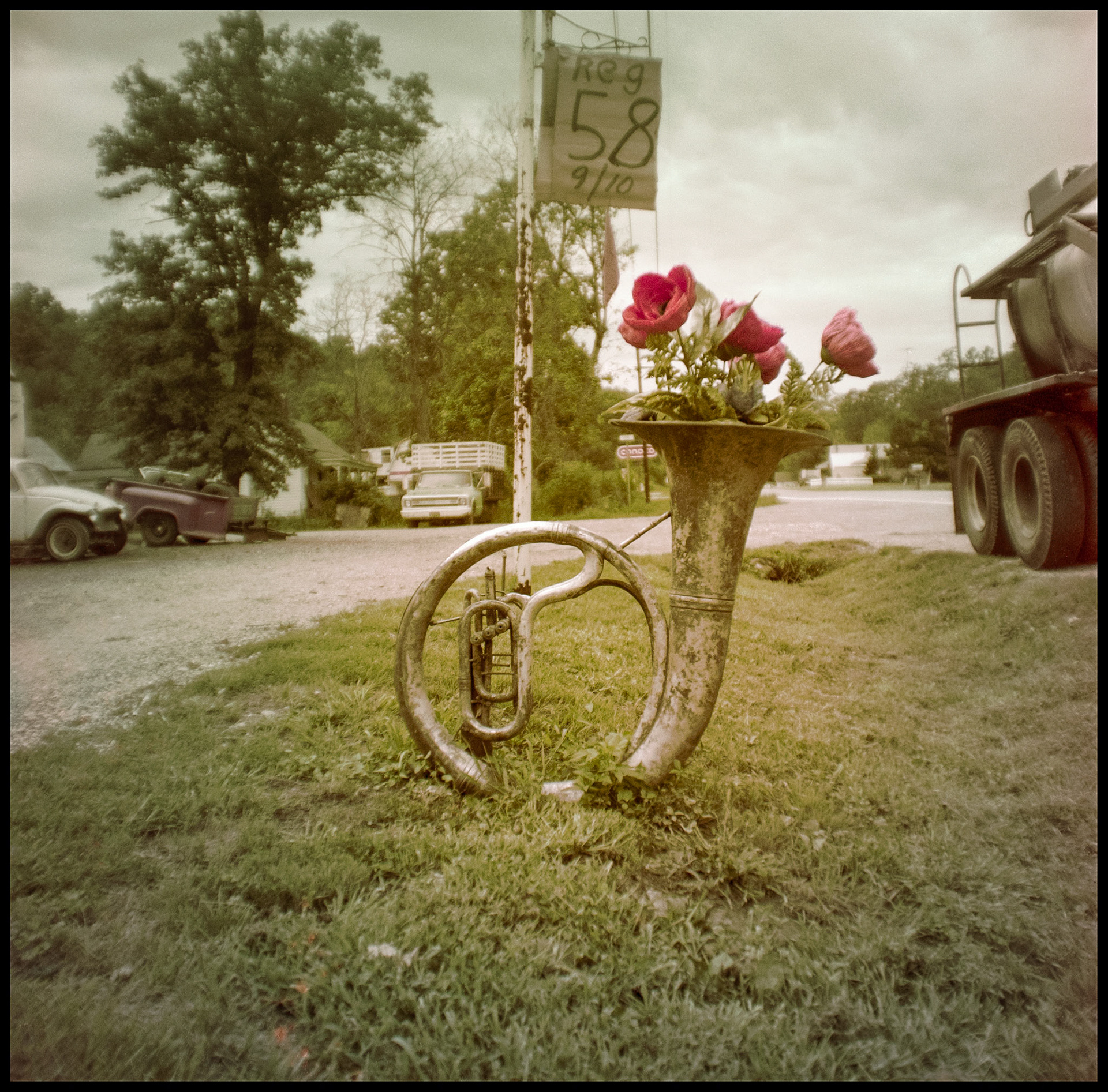A vintage image of a novelty Sousaphone planter festooned with plastic flowers in front of a Missouri Ozark mom and pop gas station in 1977.
