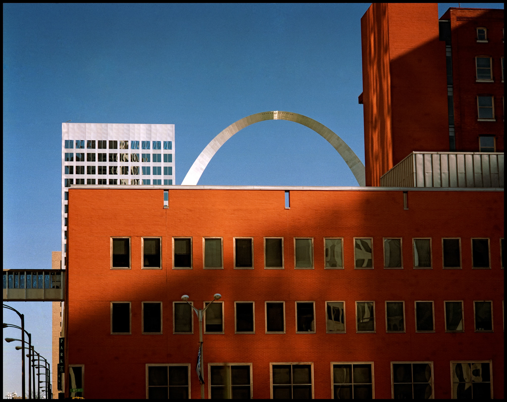 A vintage minimialistic abstract urbanscape detail view of a red brick office building obscuring most of the Gateway Arch in St. Louis, Missouri USA, 1988.