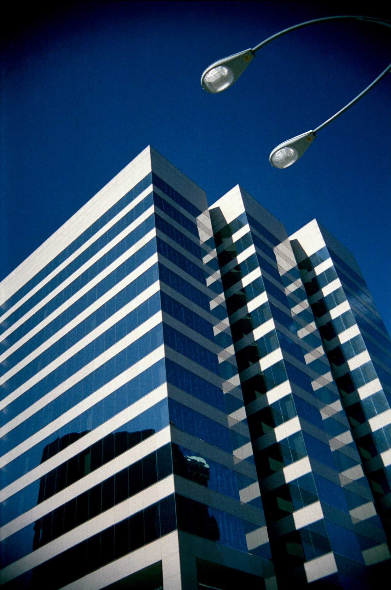 A minimal abstract view of the Peabody Building in downtown St. Louis with mirrored windows and streetlight looming overhead. Part of An Afternoon in St. Louis series, St. Louis, Missouri, 1988.