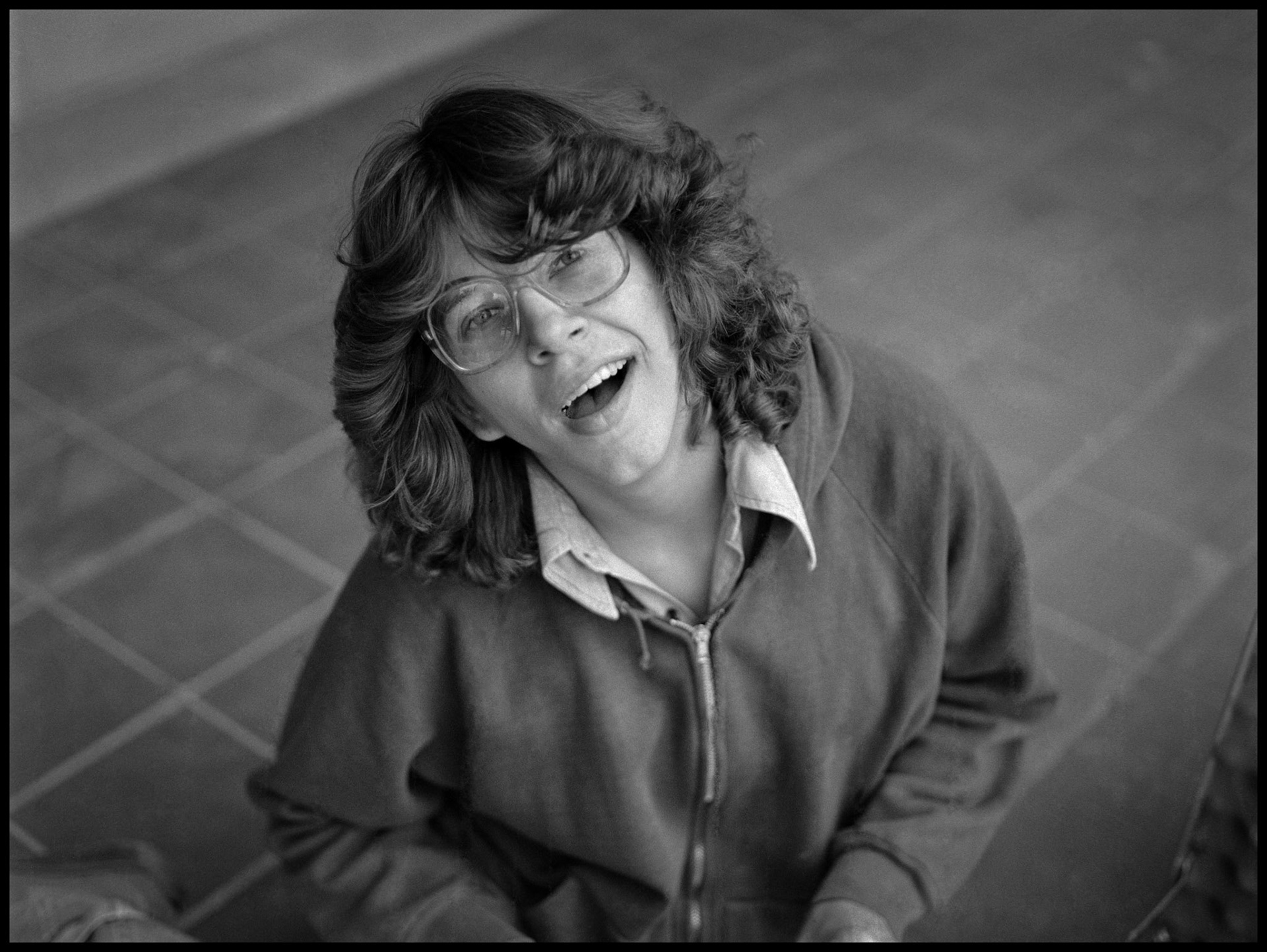 A 1980's vintage portrait of a young woman sitting on a tile walk looking up with a expression of surprise. Kirksville, Missouri 1981