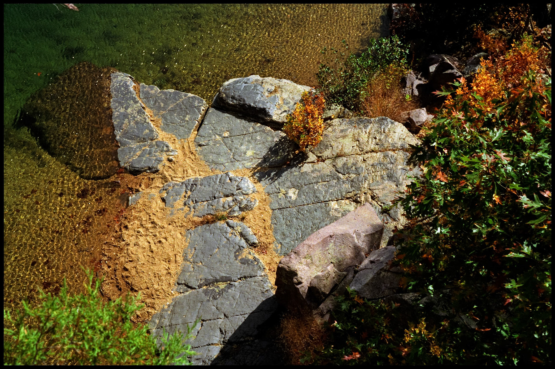 A minimalistic abstract overhead image of a multi-colored granite outcropping with sand and Autumn leaves at edge of the Black River at Johnson's Shut-Ins State Park before the flood of 2005 when Taum Sauk Resevoir failed. Near Lesterville, Missouri USA, 1992.
