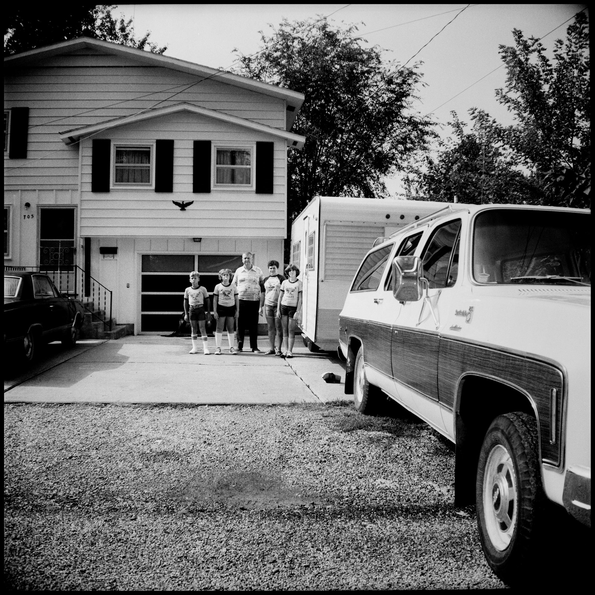A family posing next to their travel trailer in front of their house before heading out on Summer vacation.  Kirksville, Missouri 1977