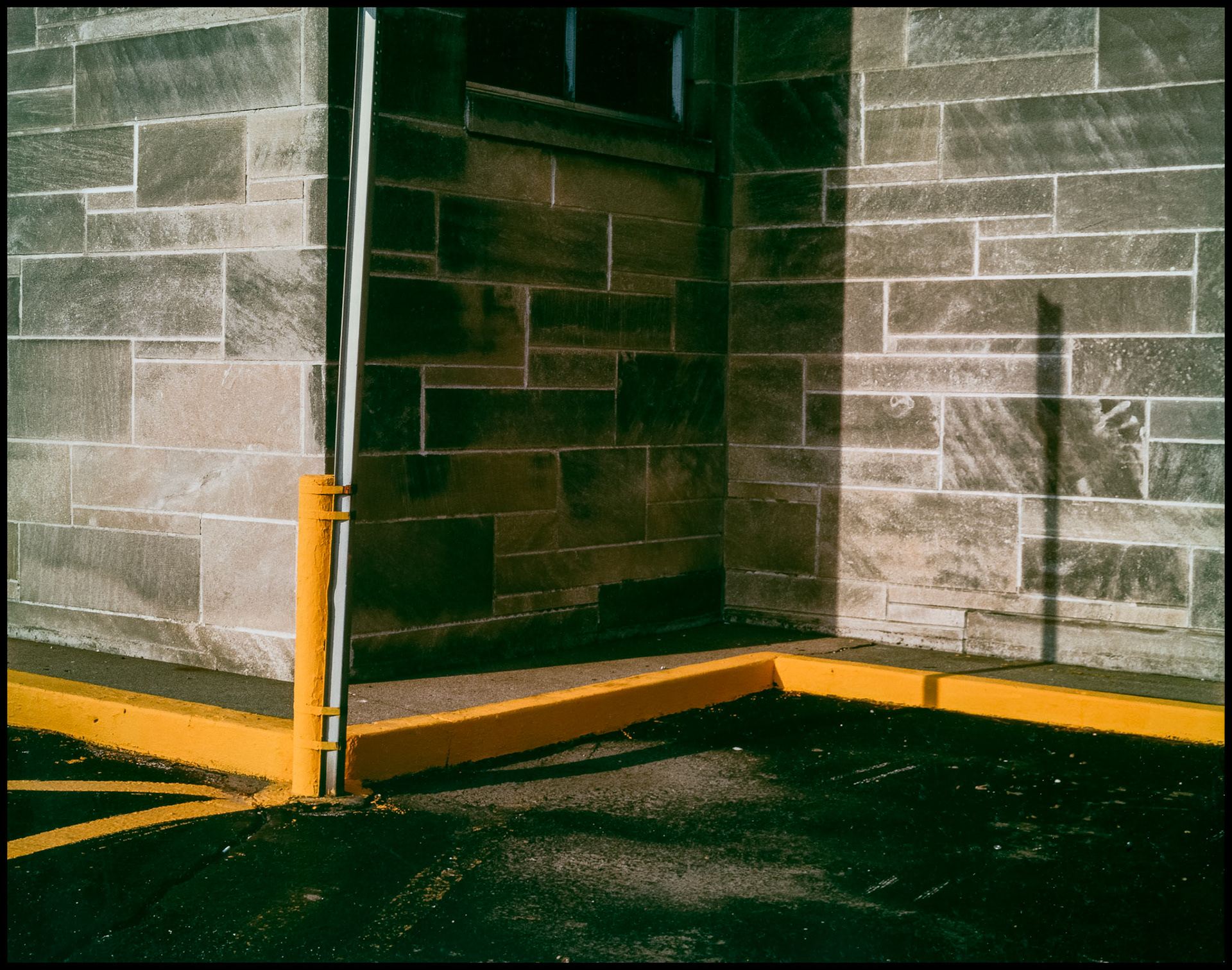 A minimal abstract geometric study of the detail of a post office wall and parking curbs, safety bollard, and shadow. Bloomington, Indiana 1986