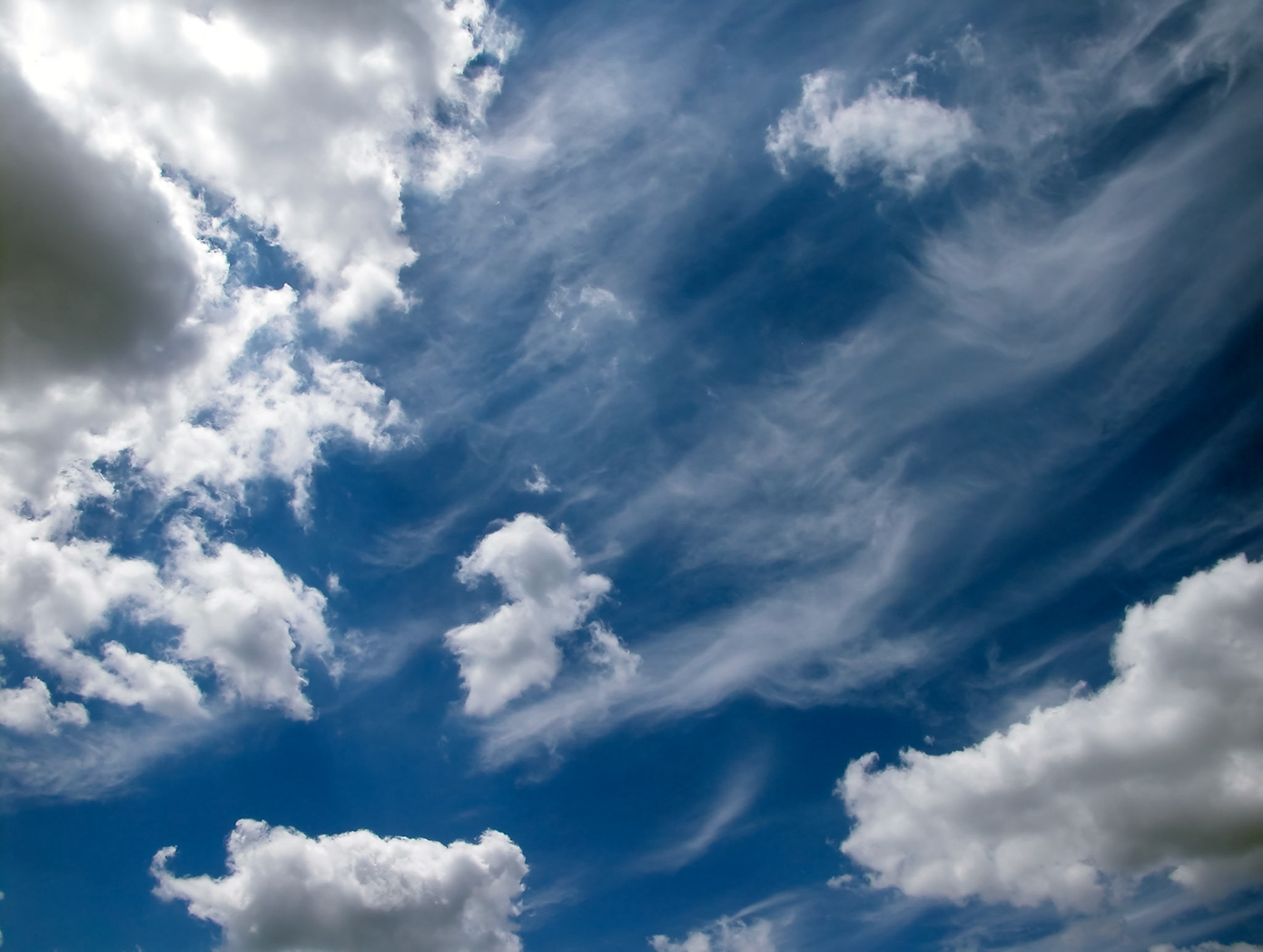 Whispy cirrus clouds shooting out diagonally behind stratus clouds contrasted by a dark blue sky in Centralia Missouri