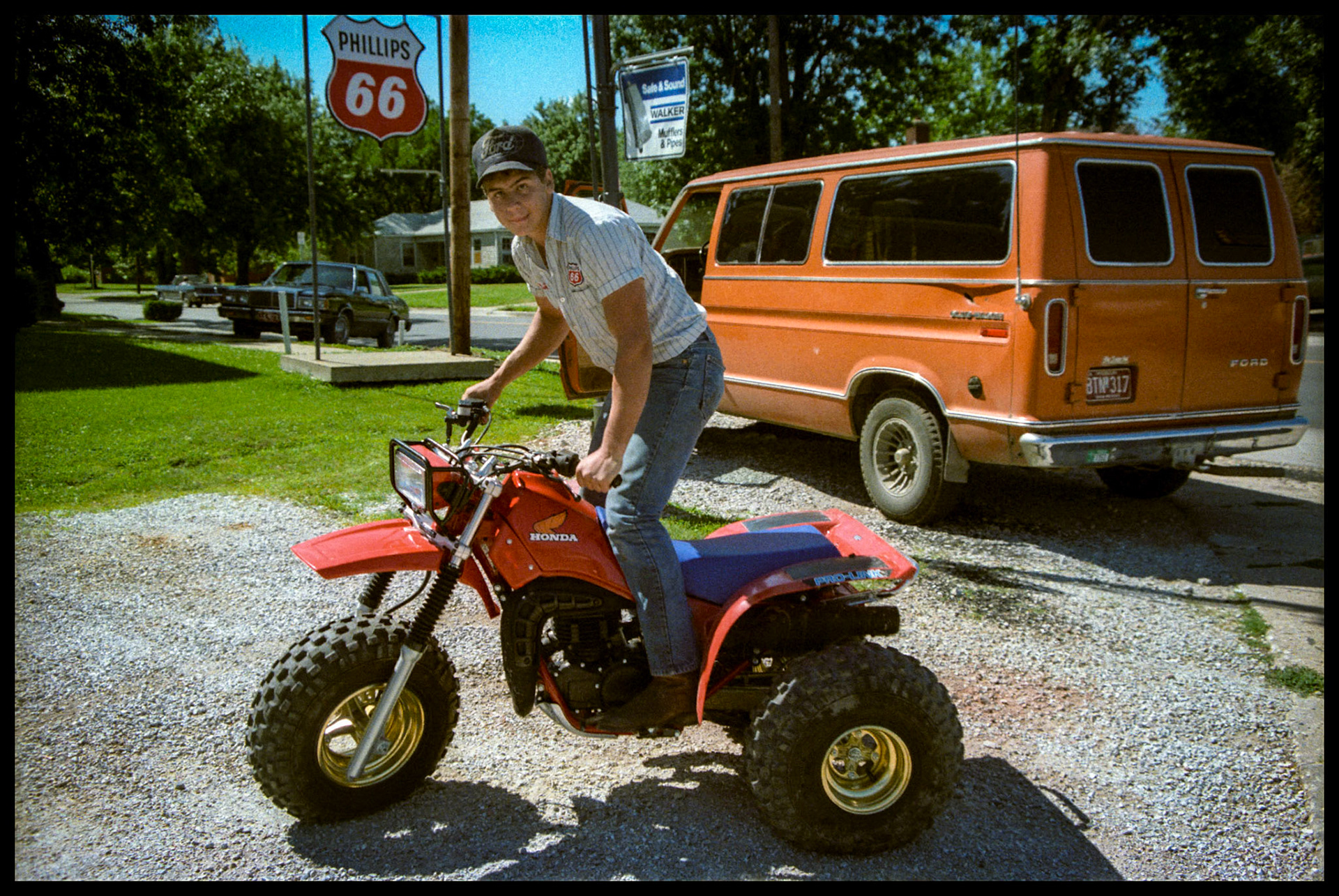 A 1980's vintage portrait of a teenage boy posing with his new "3-wheeler" ATV at his family service station. Kirksville, Missouri 1984