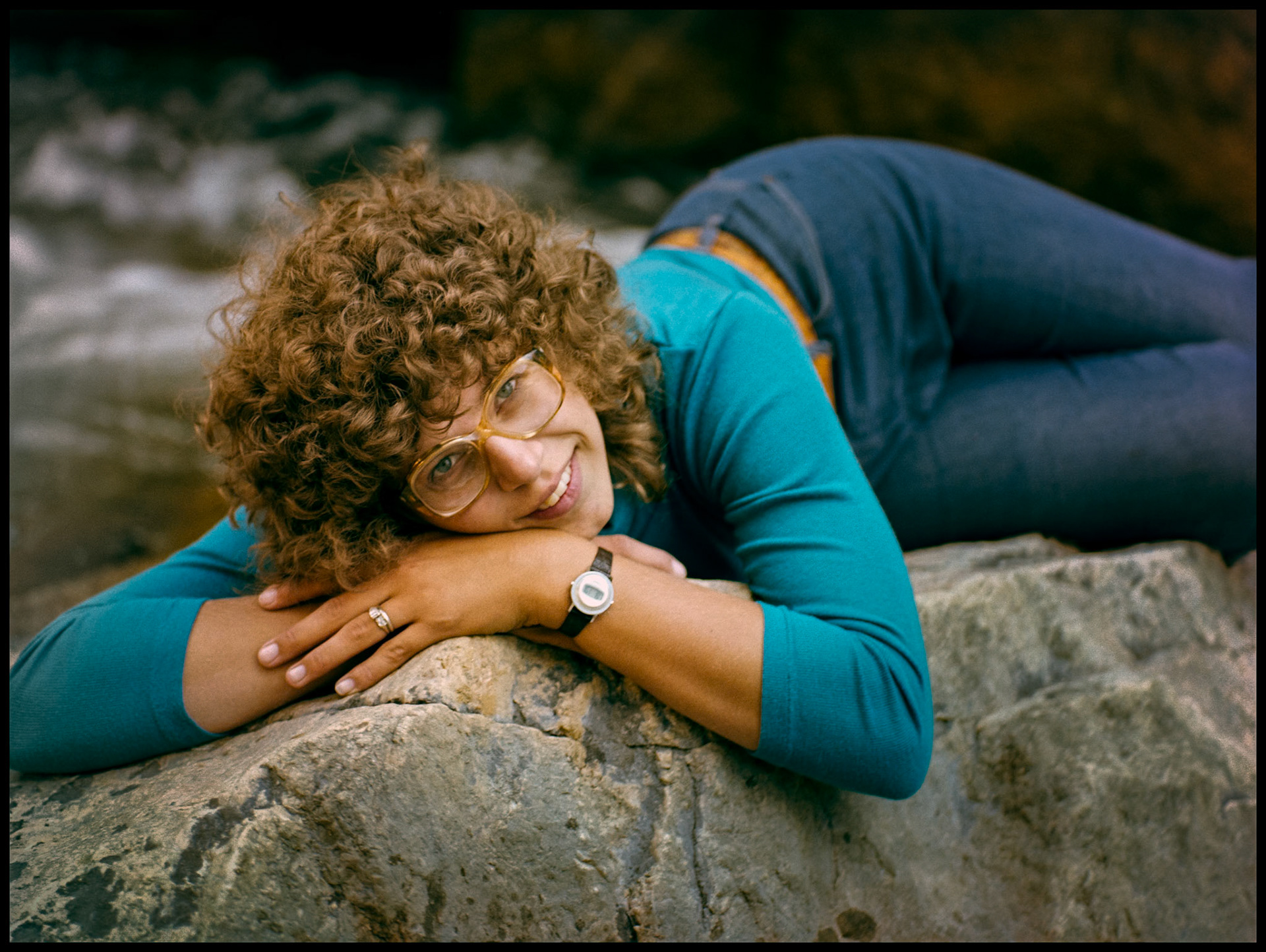 A 1980's vintage portrait of a young woman laying on a boulder next to a creek. Near Almont, Colorado 1981