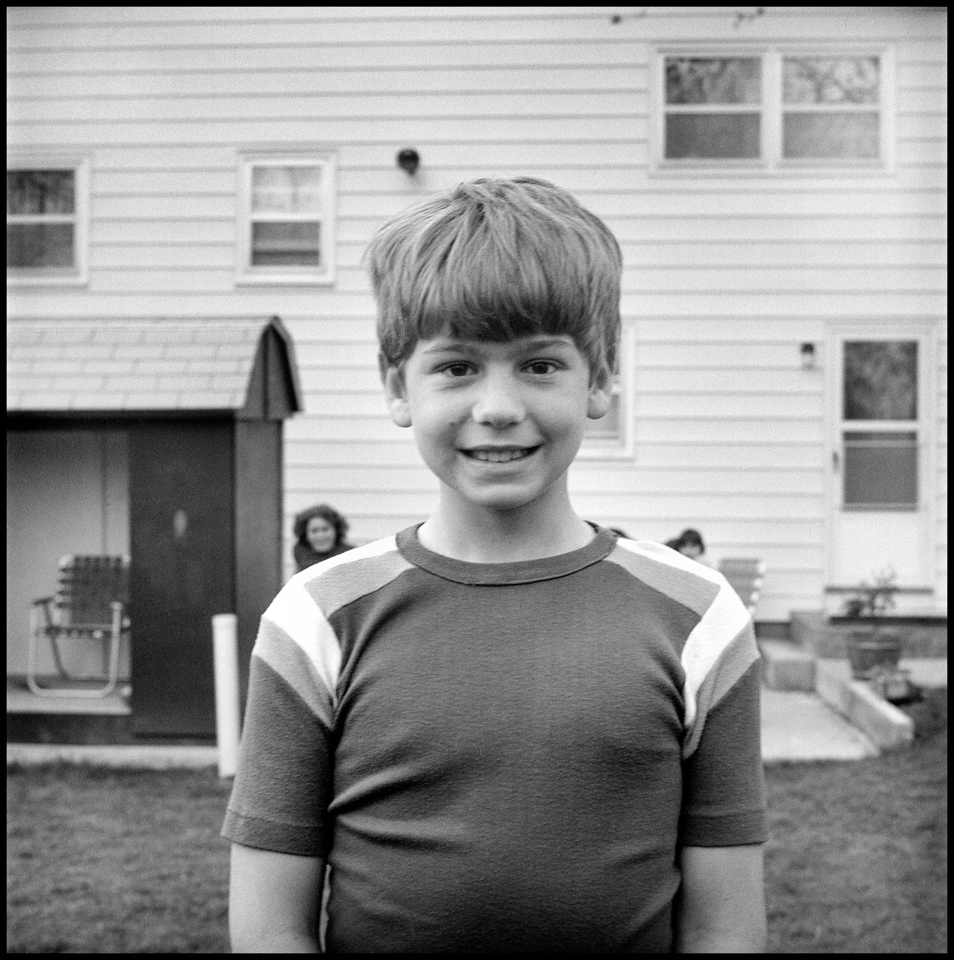 A vintage image of a boy posing for his brother in his back yard as his sisters observe, Kirksville, Missouri 1978