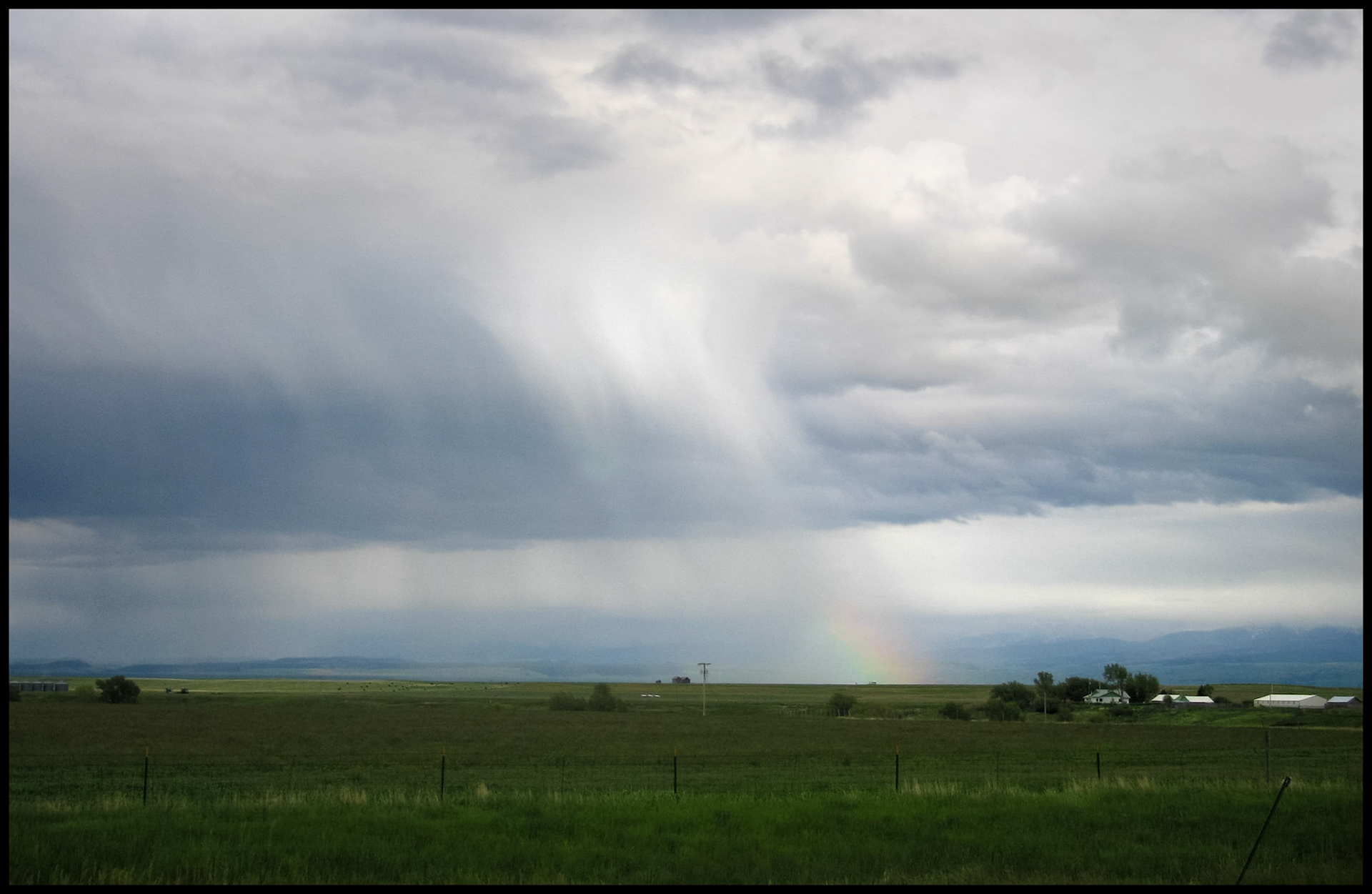 Rain downpour streaks. coming down from the grey clouds of an approaching storm with a little rainbow at the gound in a Colorado mountain valley. 2005