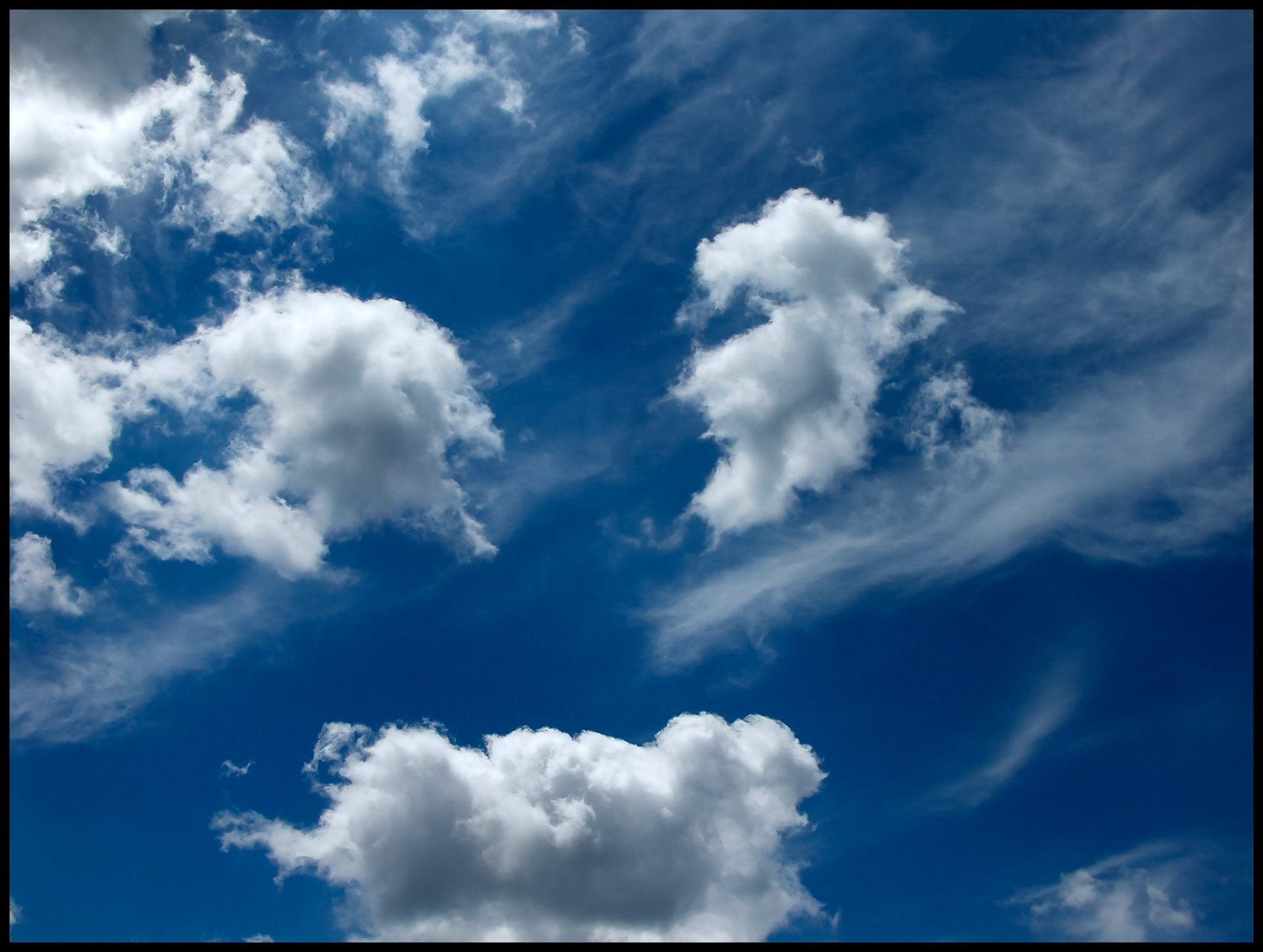 Whispy cirrus clouds shooting out diagonally behind stratus clouds contrasted by a dark blue sky in Centralia Missouri