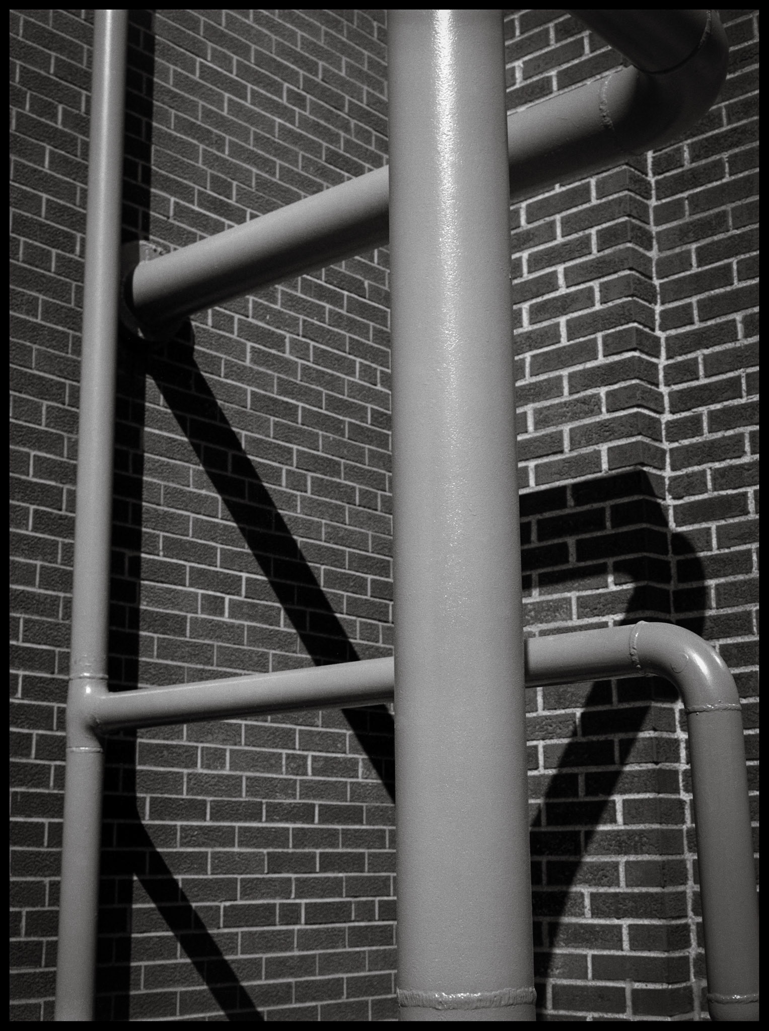 A minimal abstract detail of pipes and their shadow against a brick wall on Northeast Missouri State University (Since renamed Truman State University) campus. Kirksville, Missouri 1981