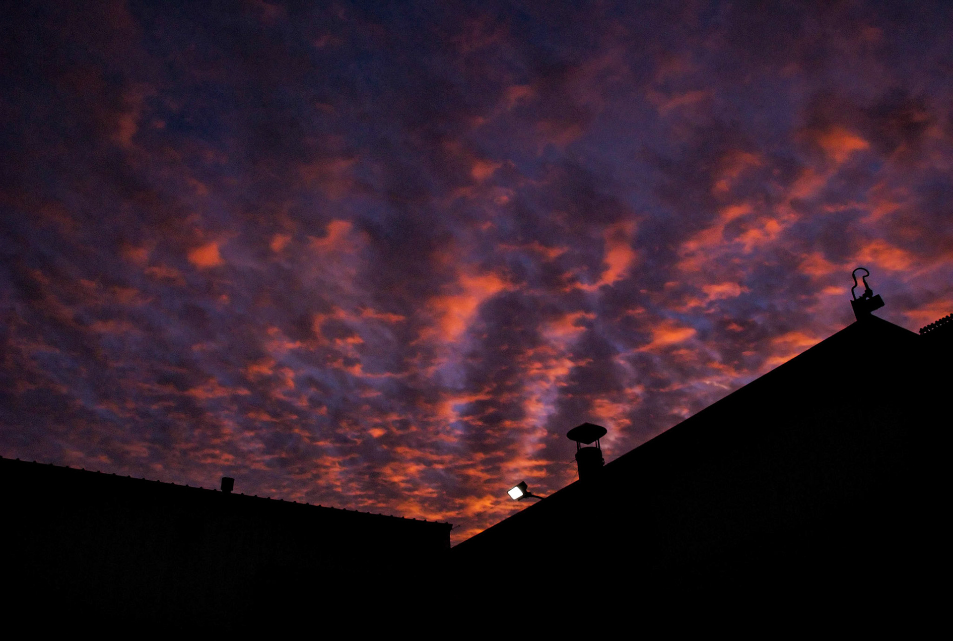 A colorful sunset accents rows of textured clouds over the silhouetted shape of a factory building with a single floodlight. Centralia, Missouri, 2008.