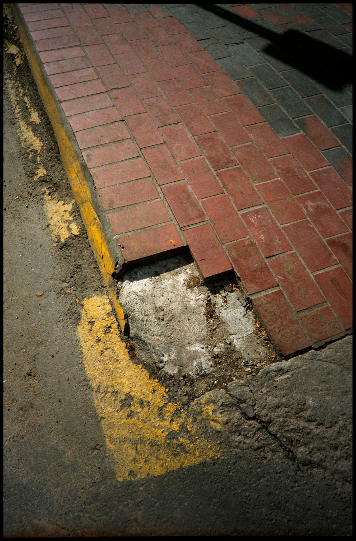 Missing bricks on a sidewalk accented with yellow paint and the shadow of a traffic sign in Santa Fe New Mexico USA 1993