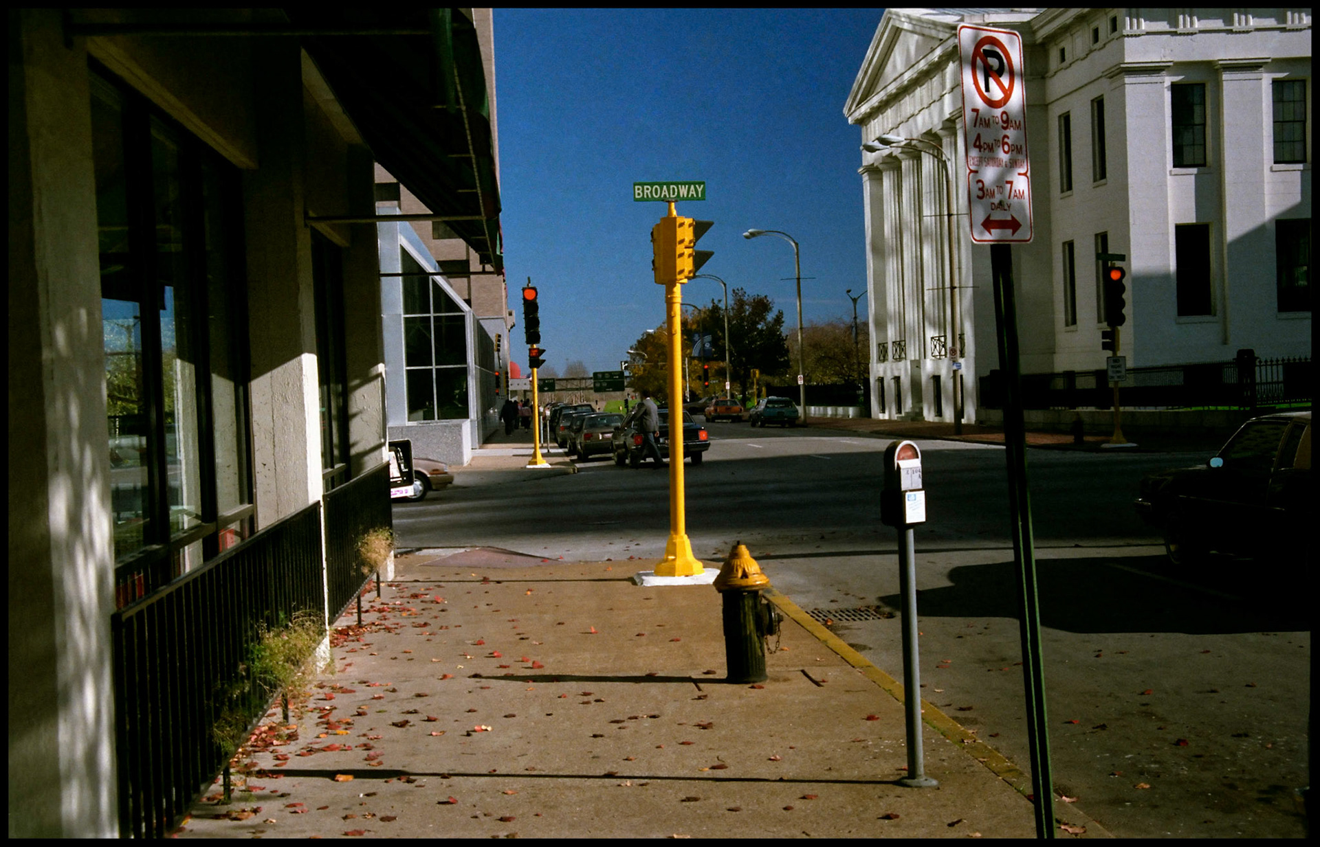 A vintage urban street scene of downtown St. Louis Missouri in 1988 featuring a brightly sunlit yellow stoplight surrounded by a fire hydrant, parking meter, and various street signs.