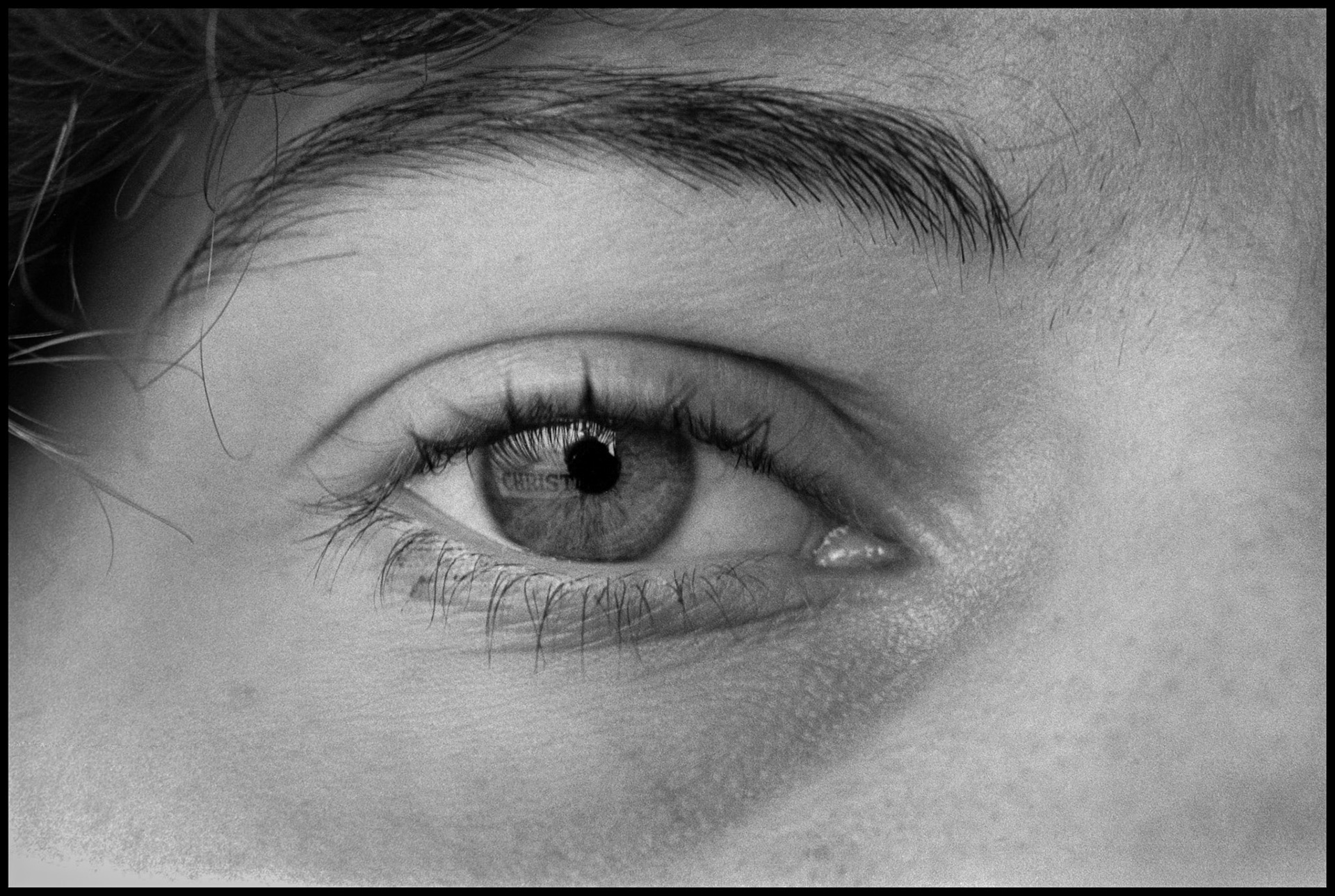 A conceptual close up of a woman's eye with the word Christ reflected in it from a Christmas decoration. Kirksville, Missouri 1980