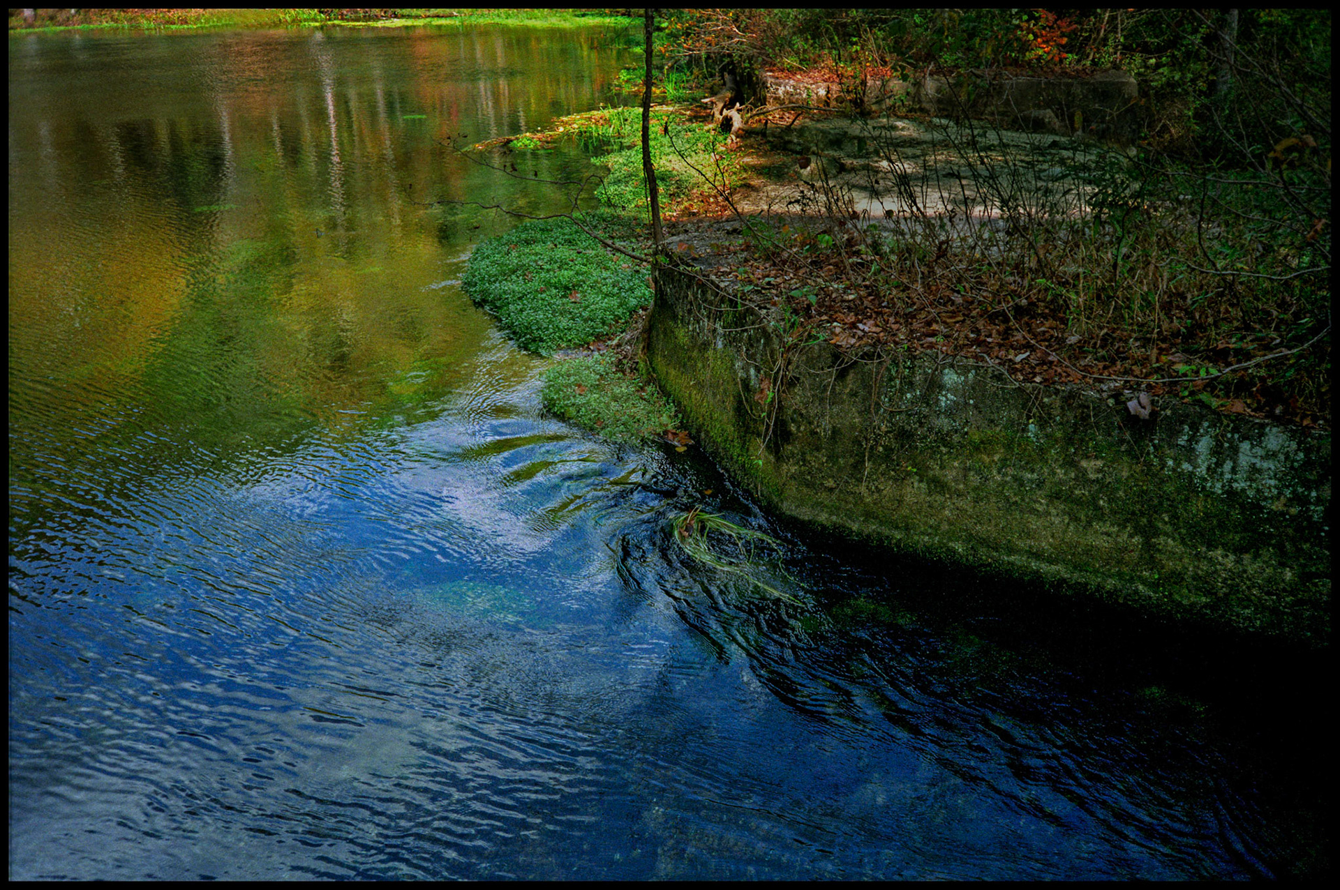 A minimal abstract detail of the brilliant colored reflections on the crystal clear water flowing into Alley Spring Mill from Alley Spring near Eminence, Missouri USA,1991