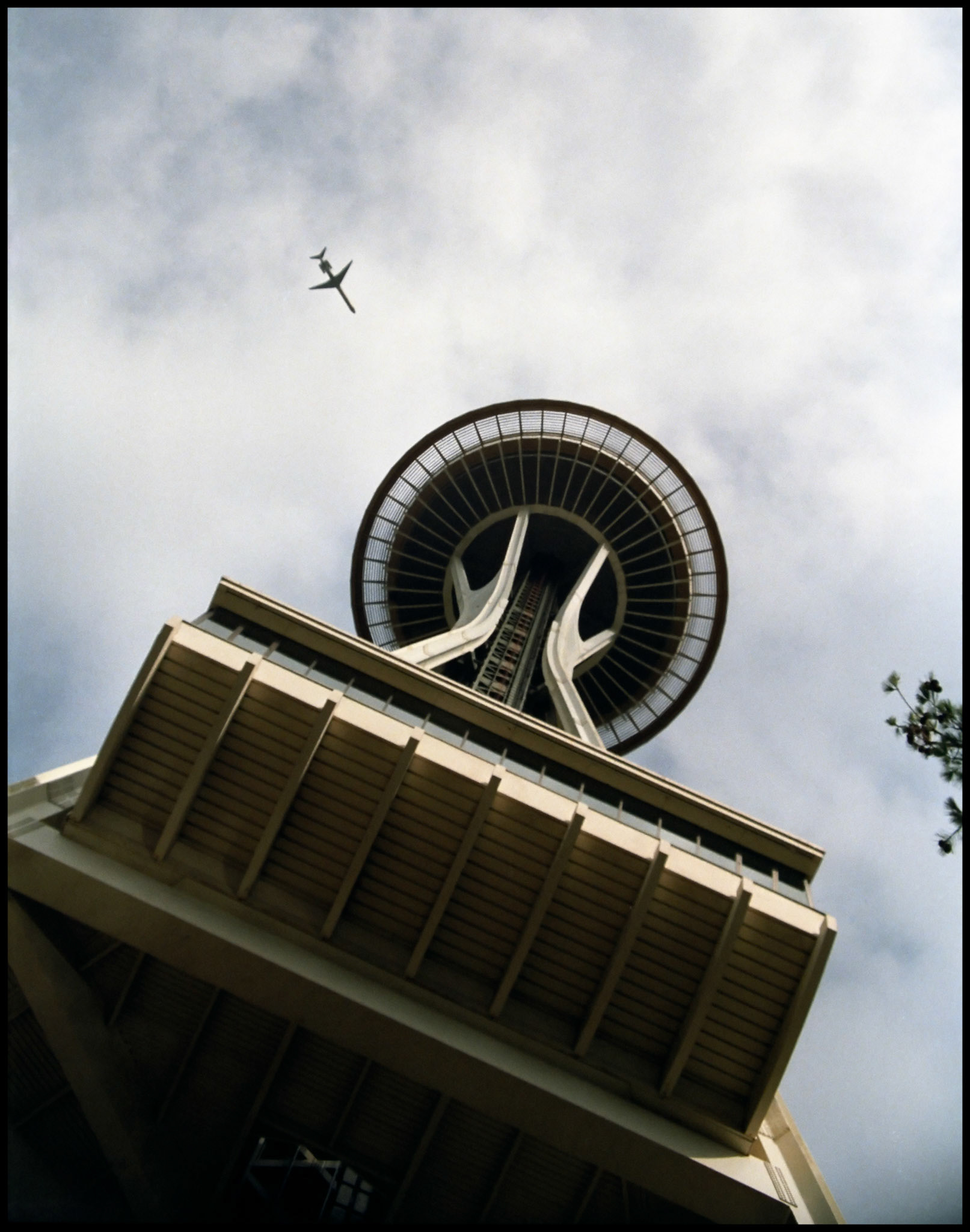 A vintage whimsical upward view from the base of the Space Needle with a passenger jet seeming to be on a collison course with it's top. Seattle Washington USA 1987