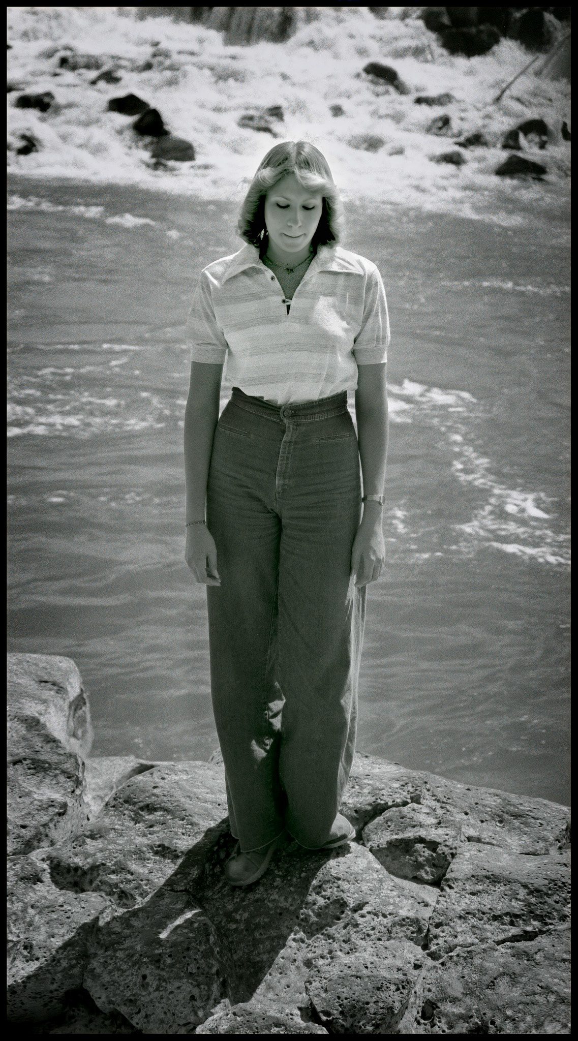 A 1970's vintage image of a young woman deep in thought standing on a rock below Idaho Falls. Idaho Falls, Idaho 1979