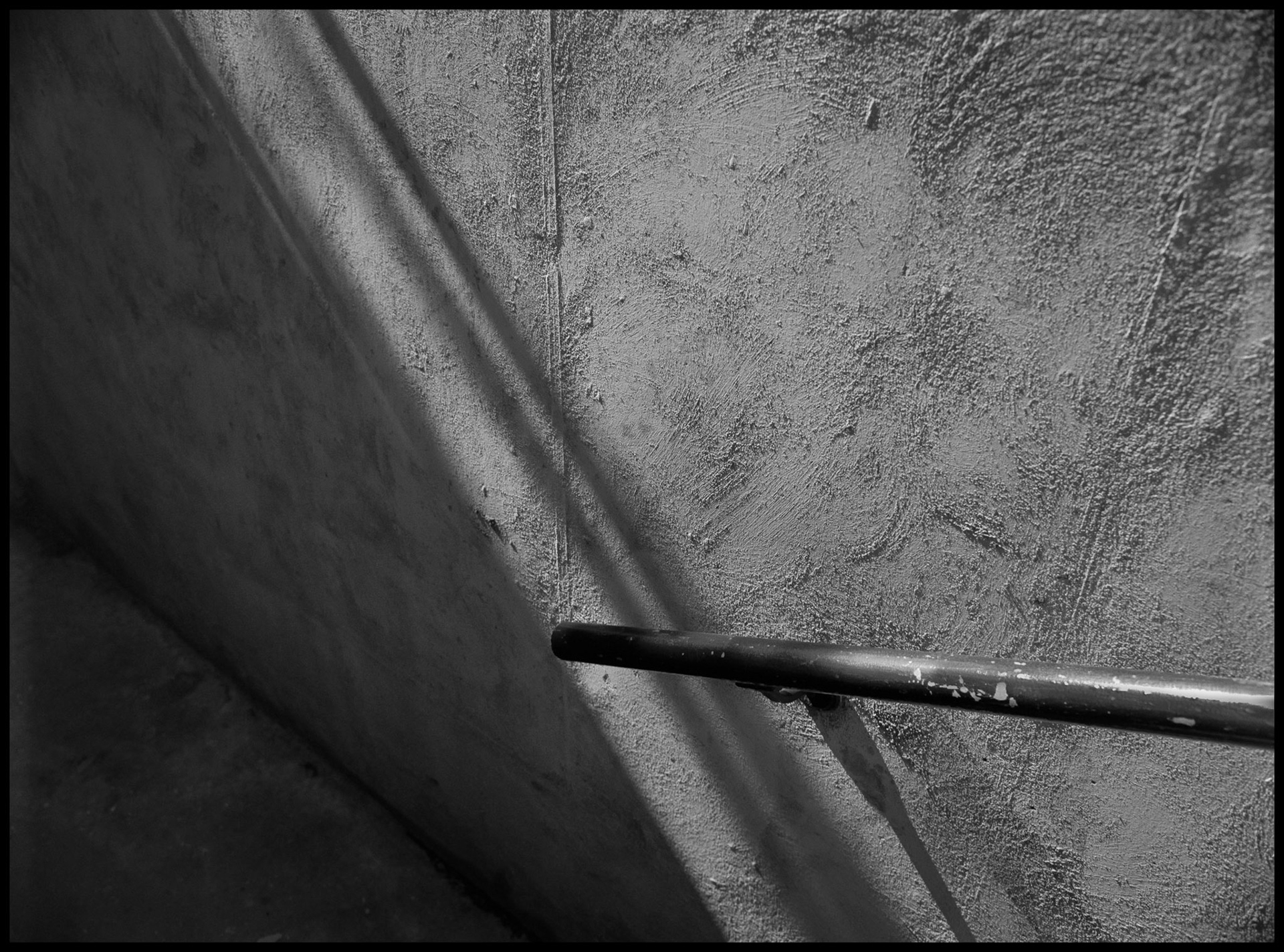 An abstract minimal detail of a stairway handrail intersecting the edge of a shadow and a seam in the concrete wall. Northeast Missouri State University (Since renamed Truman State University) Kirksville, Missouri 1981