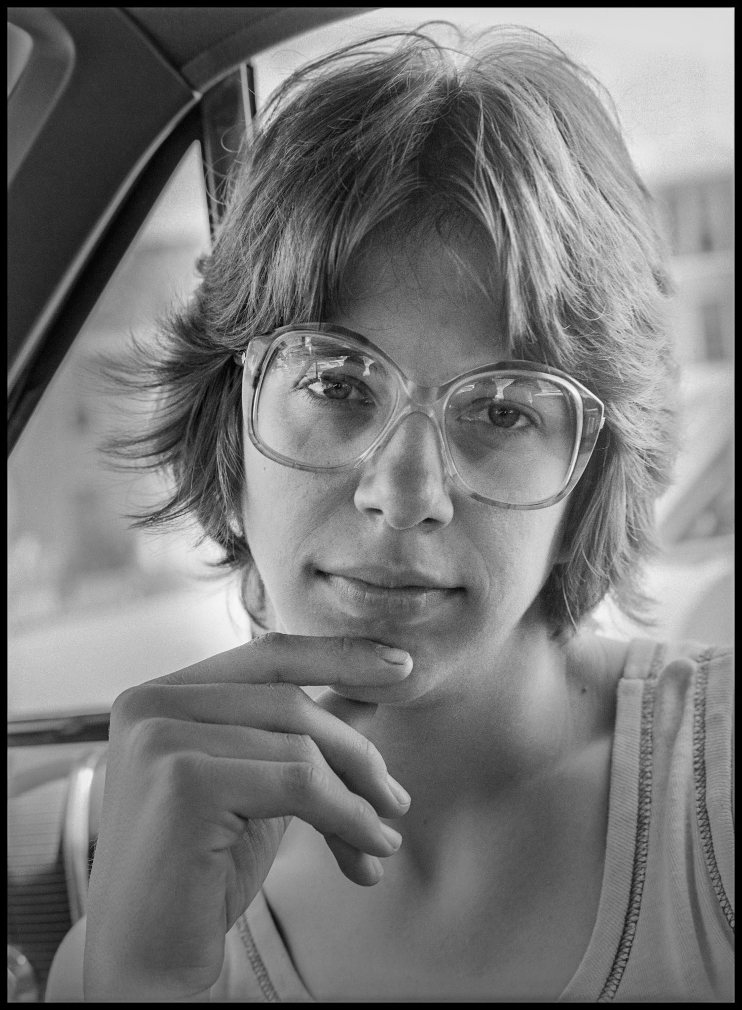 A 1980's vintage image of a young woman sitting in a car looking intently at the photographer. Kirksville, Missouri 1980