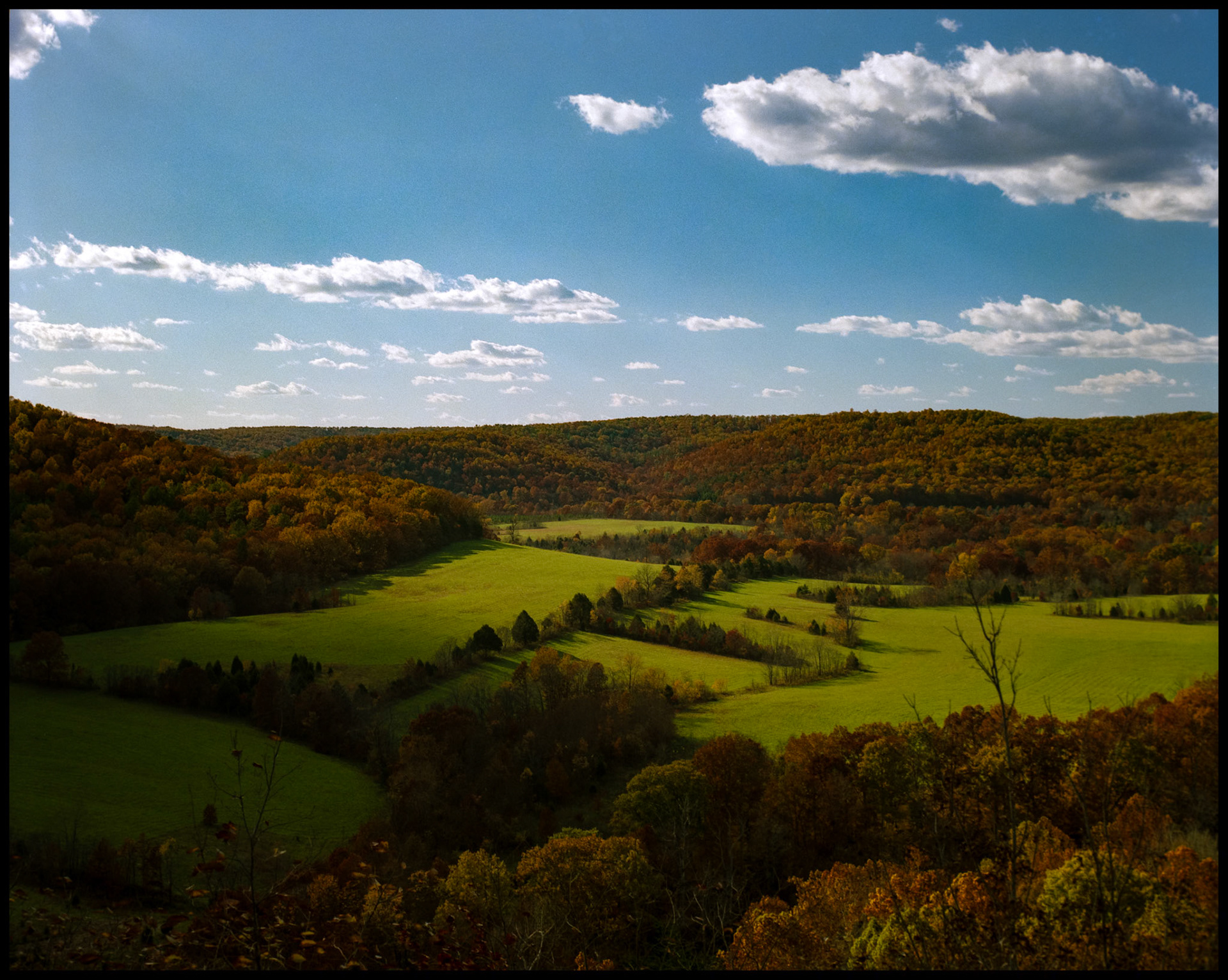 View from ridge above Akers, Missouri  and Current River on Highway K of an Ozarks meadow in Autumn with leaves beginning to turn and puffy clouds. 1988