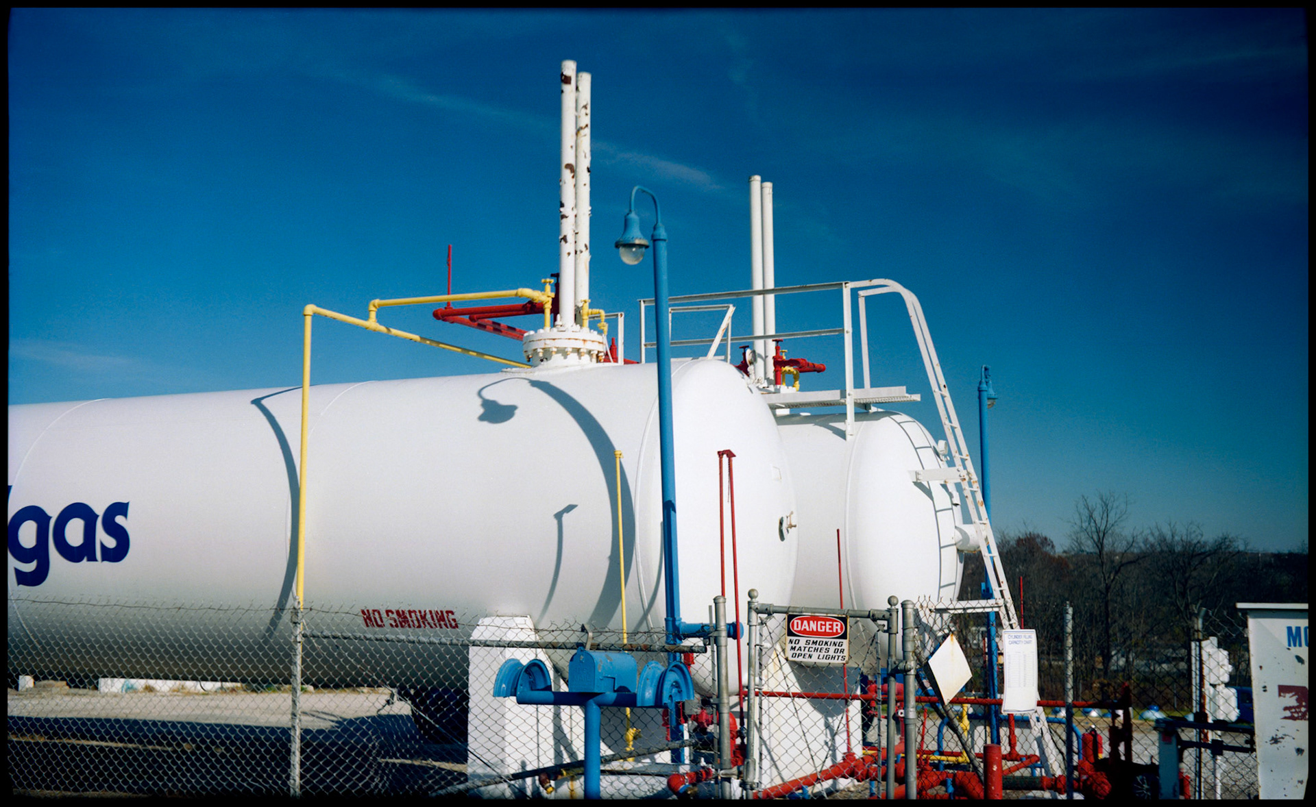 Large industrial gas tanks with colorful pipes and interesting curved shadows. Columbia, Missouri 1989