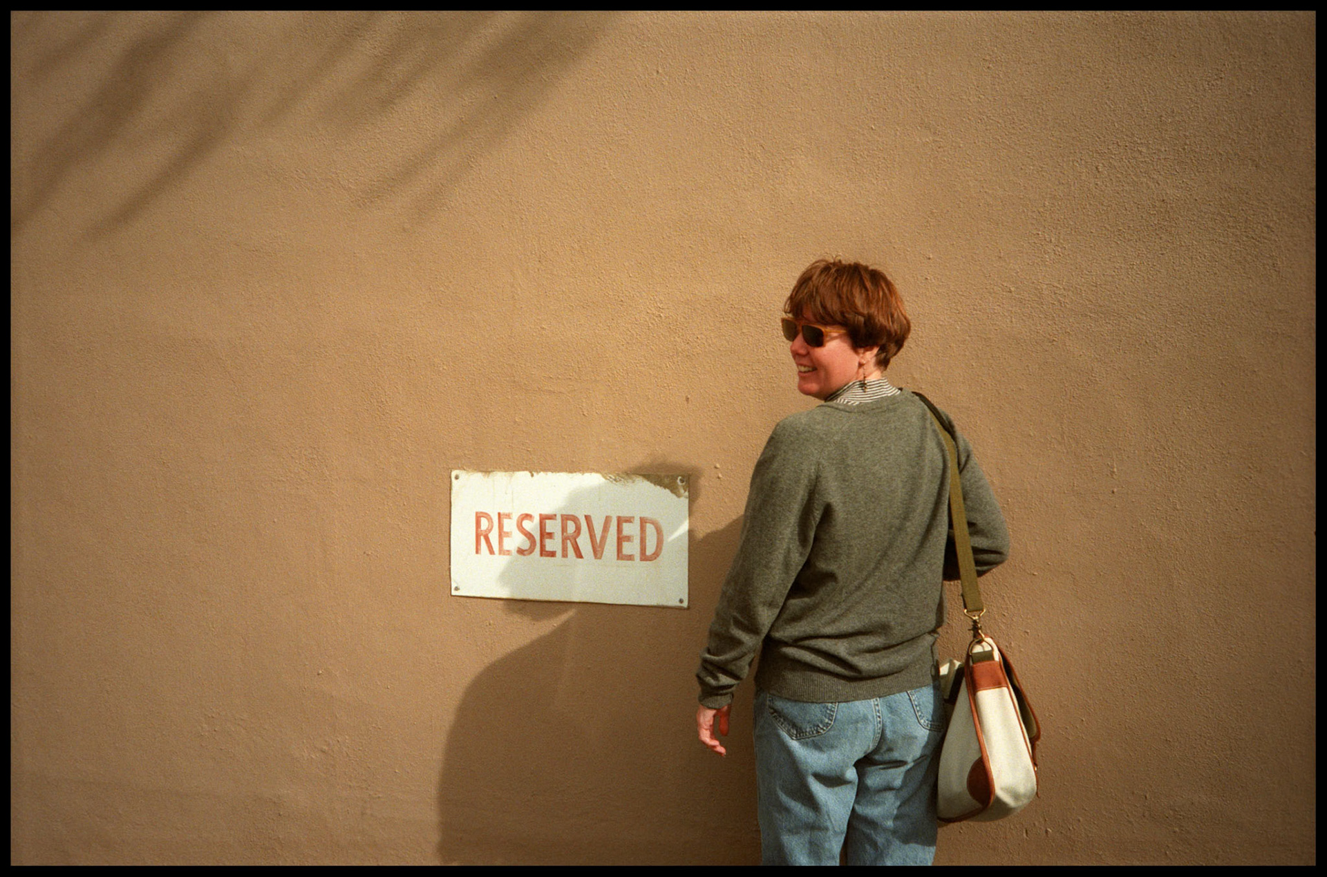 Woman standing next to a reserved sign in Santa Fe, NM looking coyly over her shoulder.