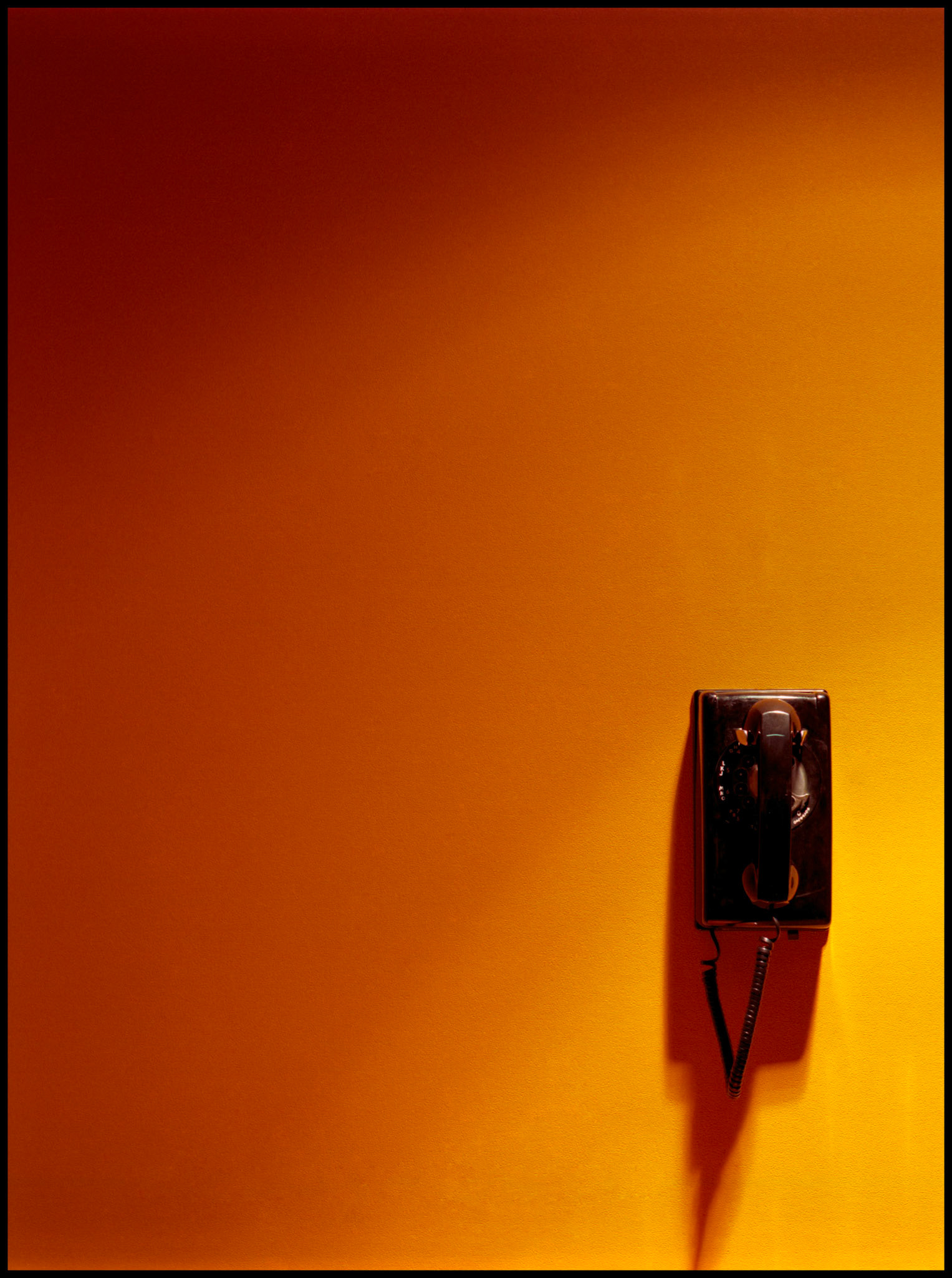 A rotary dial wall telephone on a spotlit gradated orange wall. Northeast Missouri State University (Since renamed Truman State), Baldwin Hall Art Department, Kirksville MO 1981
